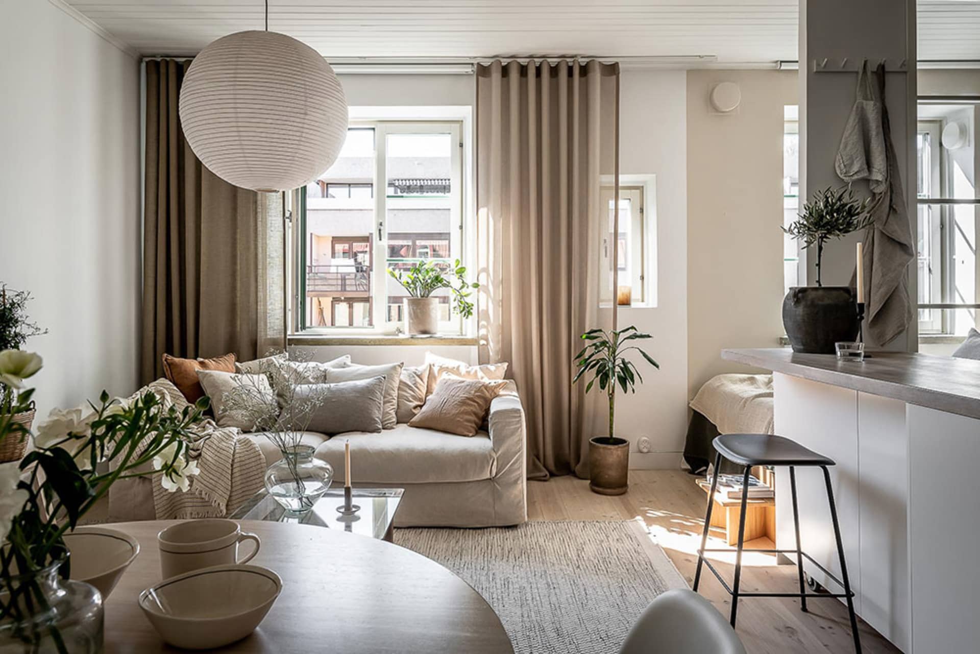A minimalist living room with a beige sofa adorned with cushions and a round glass table with bowls and mugs.