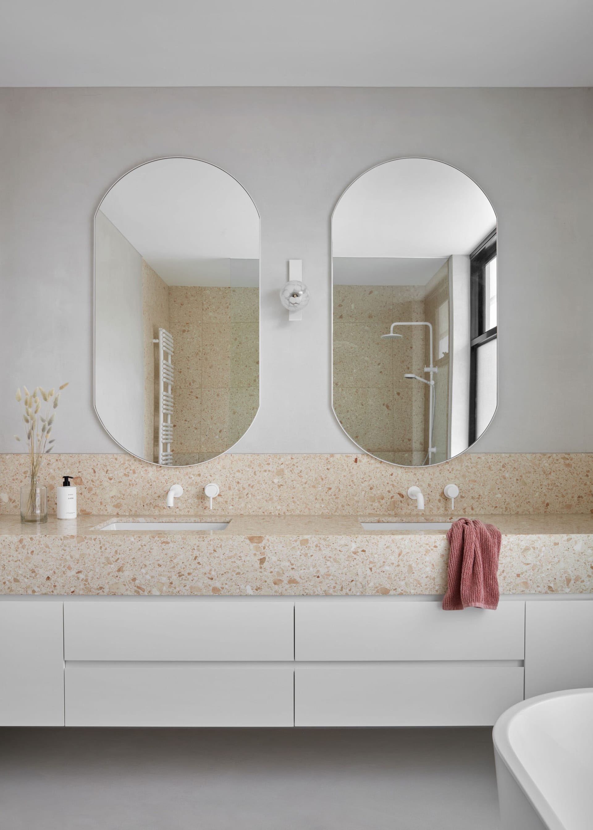 A modern bathroom featuring a terrazzo countertop with a double sink, white cabinets, and a freestanding tub in front of larg