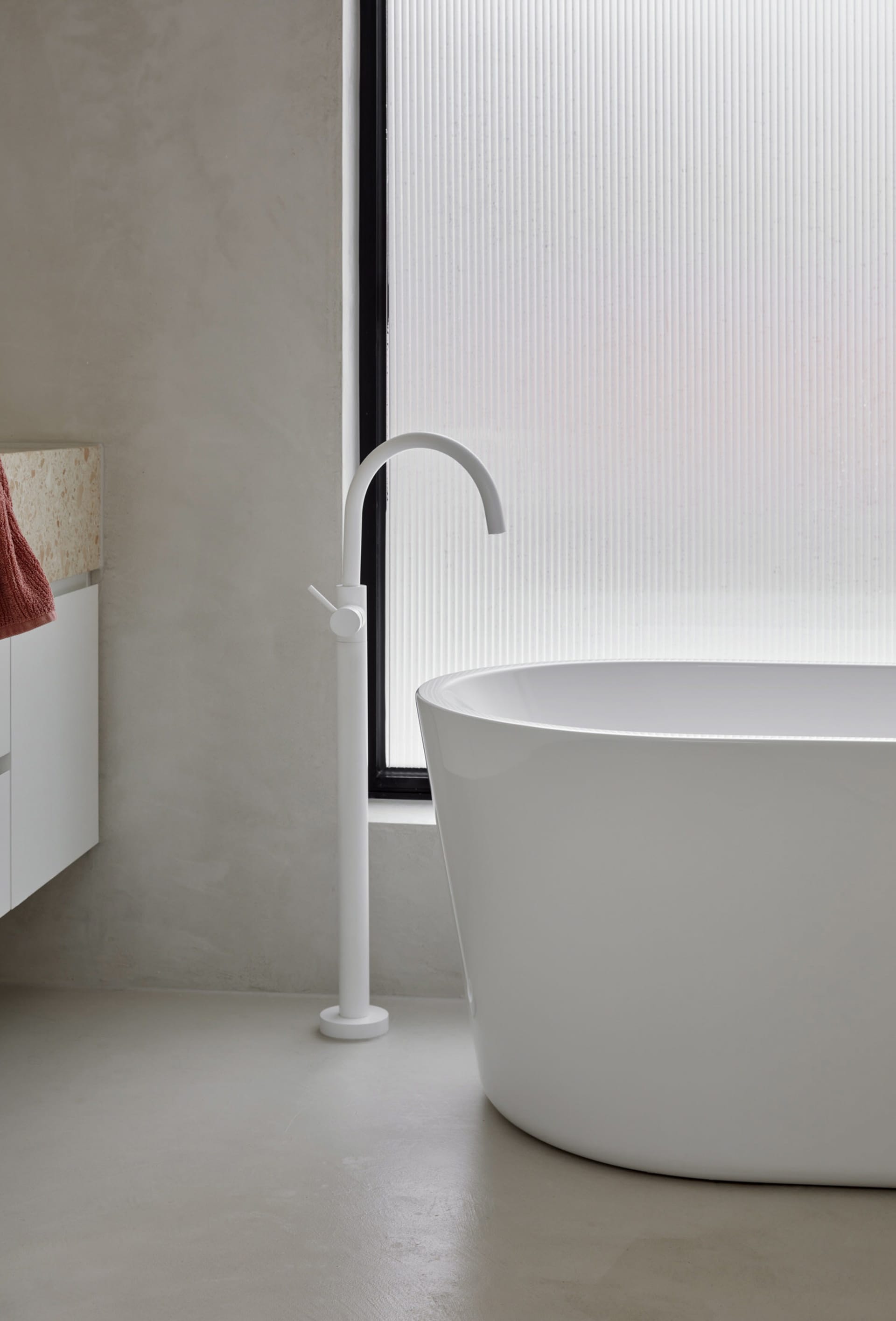 Modern minimalist bathroom featuring a white ceramic free-standing tub with a sleek, curved faucet next to a frosted window.