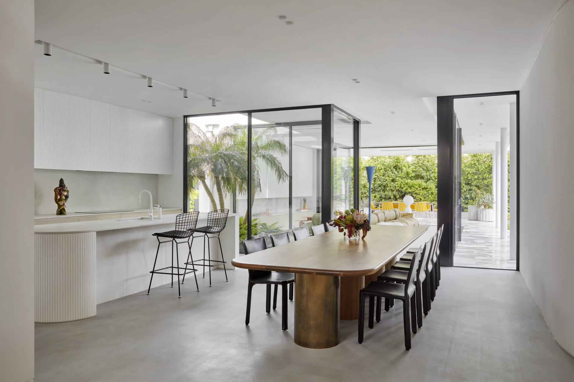 Modern dining room with transparent glass walls and a large wooden table surrounded by black chairs.
