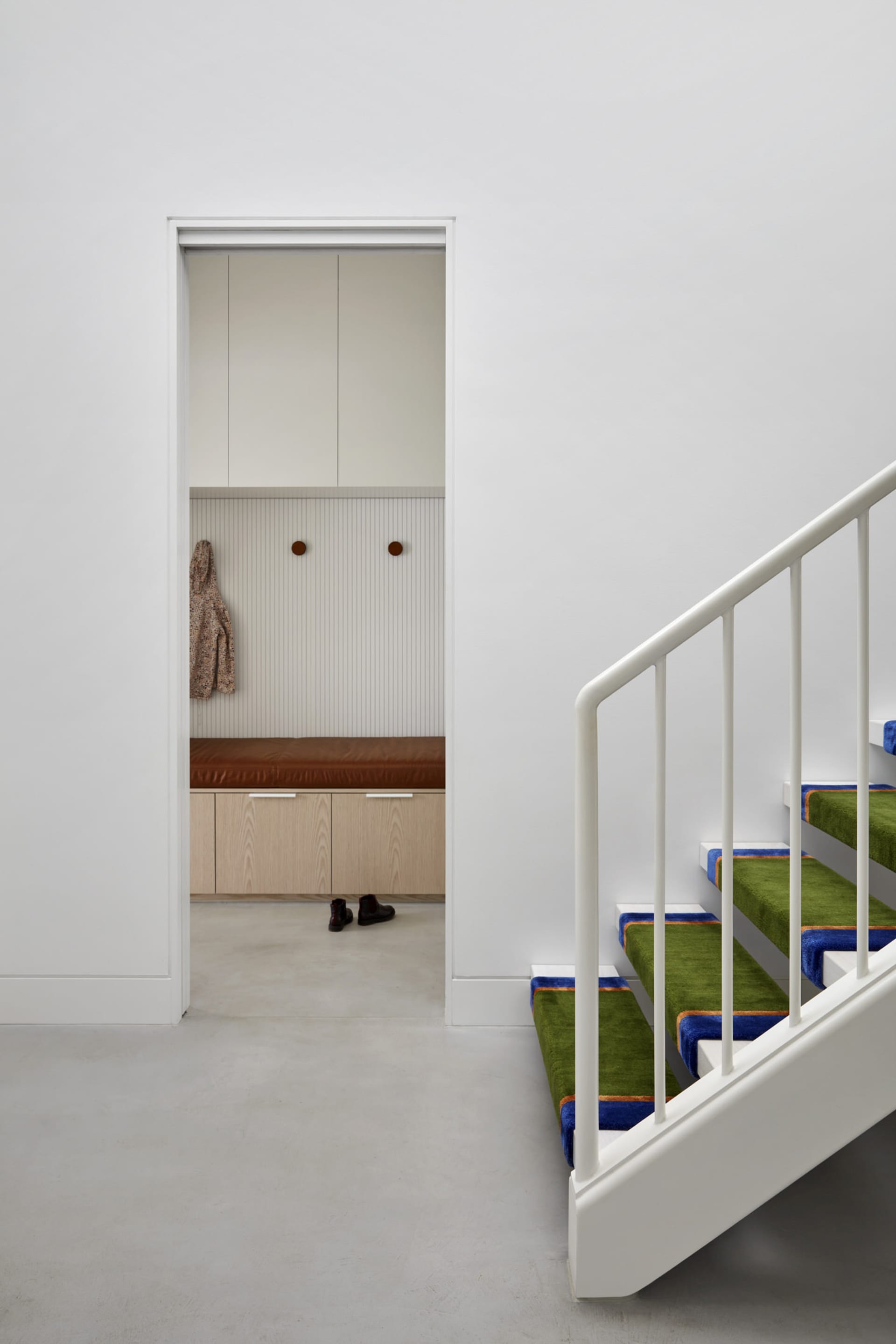 Staircase with green carpeted steps and white railings leading to an entryway with a bench and coat hooks.