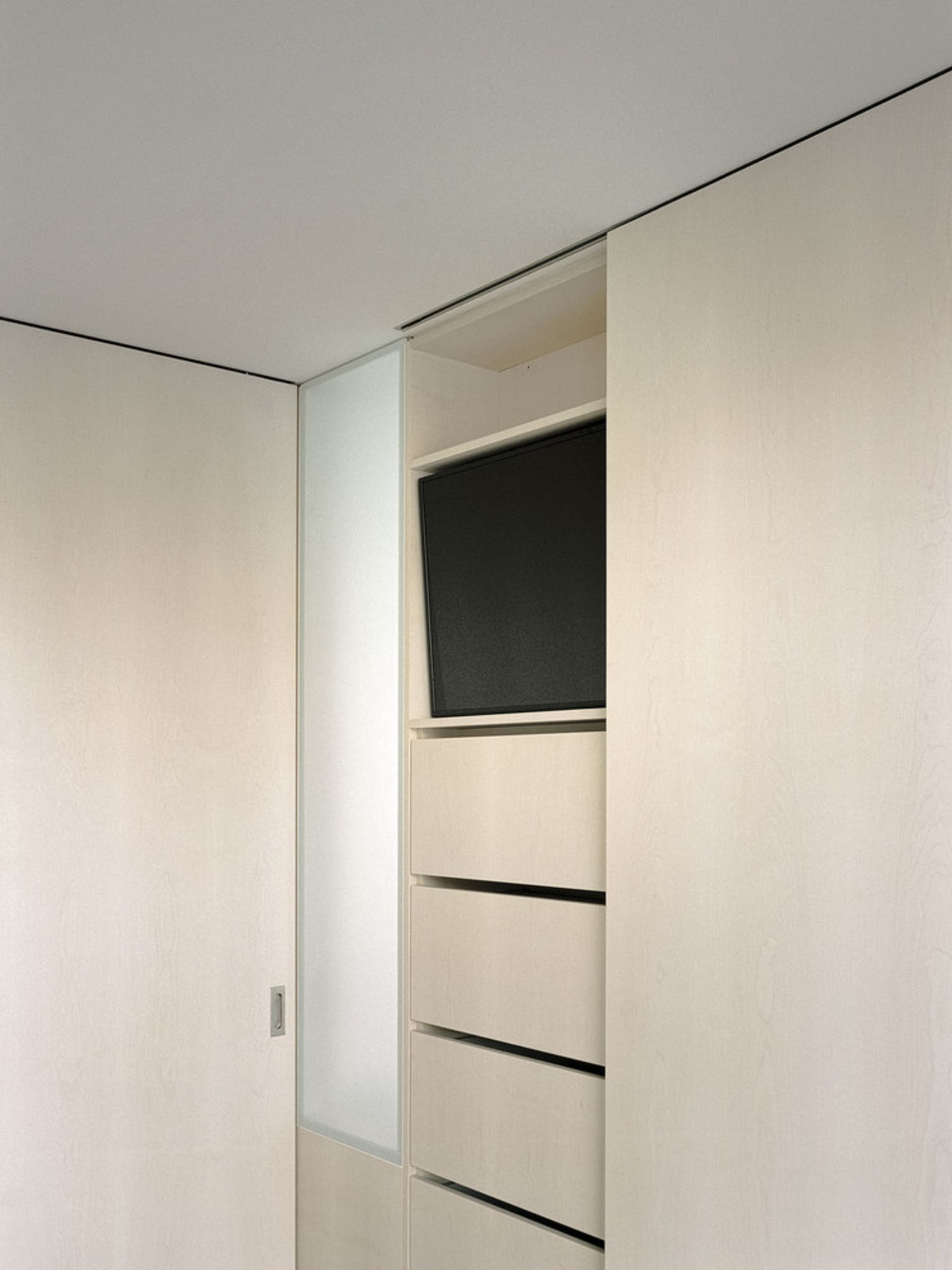 A modern minimalist closet featuring wooden drawers and a flat-screen television mounted within.