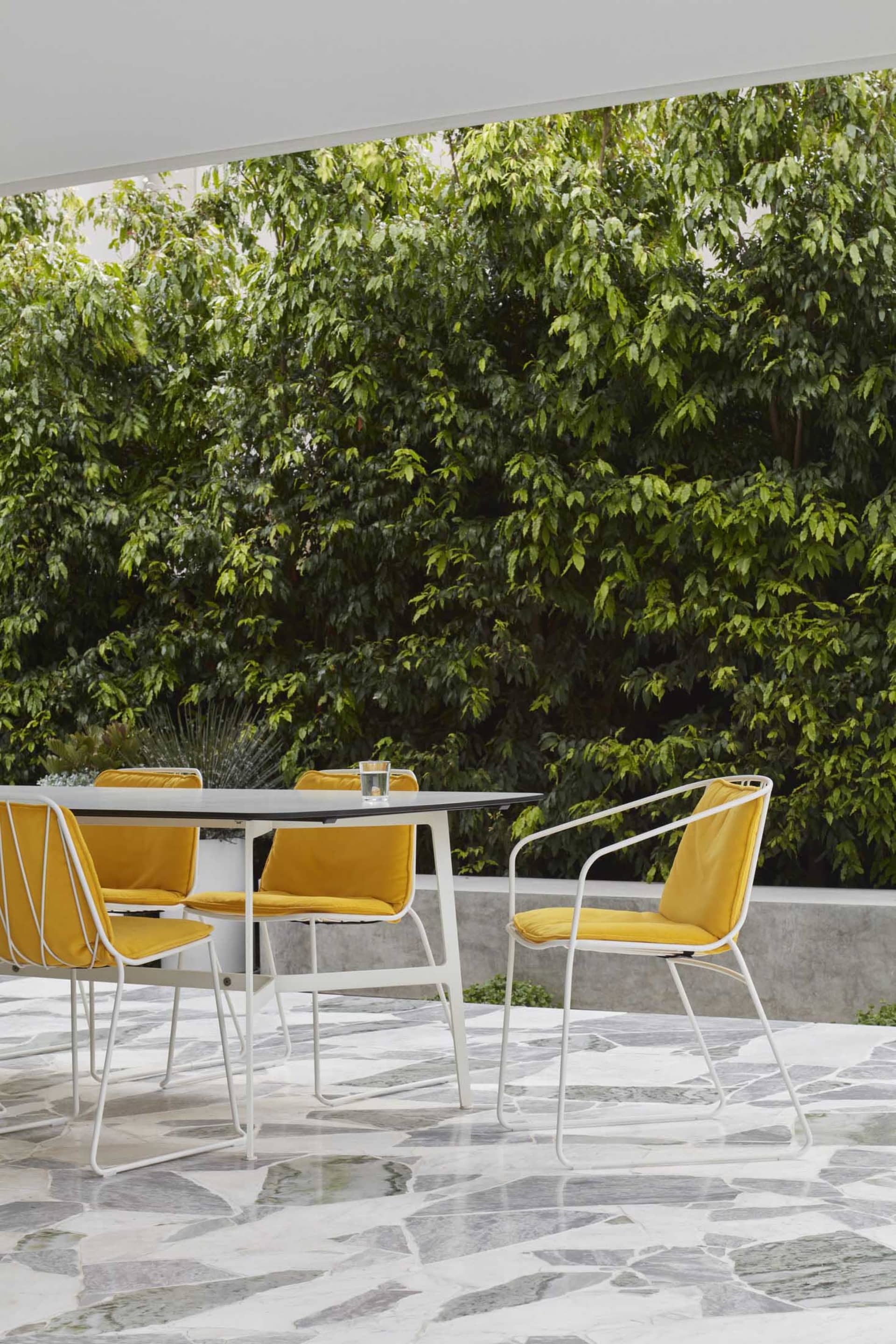 A modern outdoor seating area with yellow cushions on metal-framed chairs around a rectangular table.