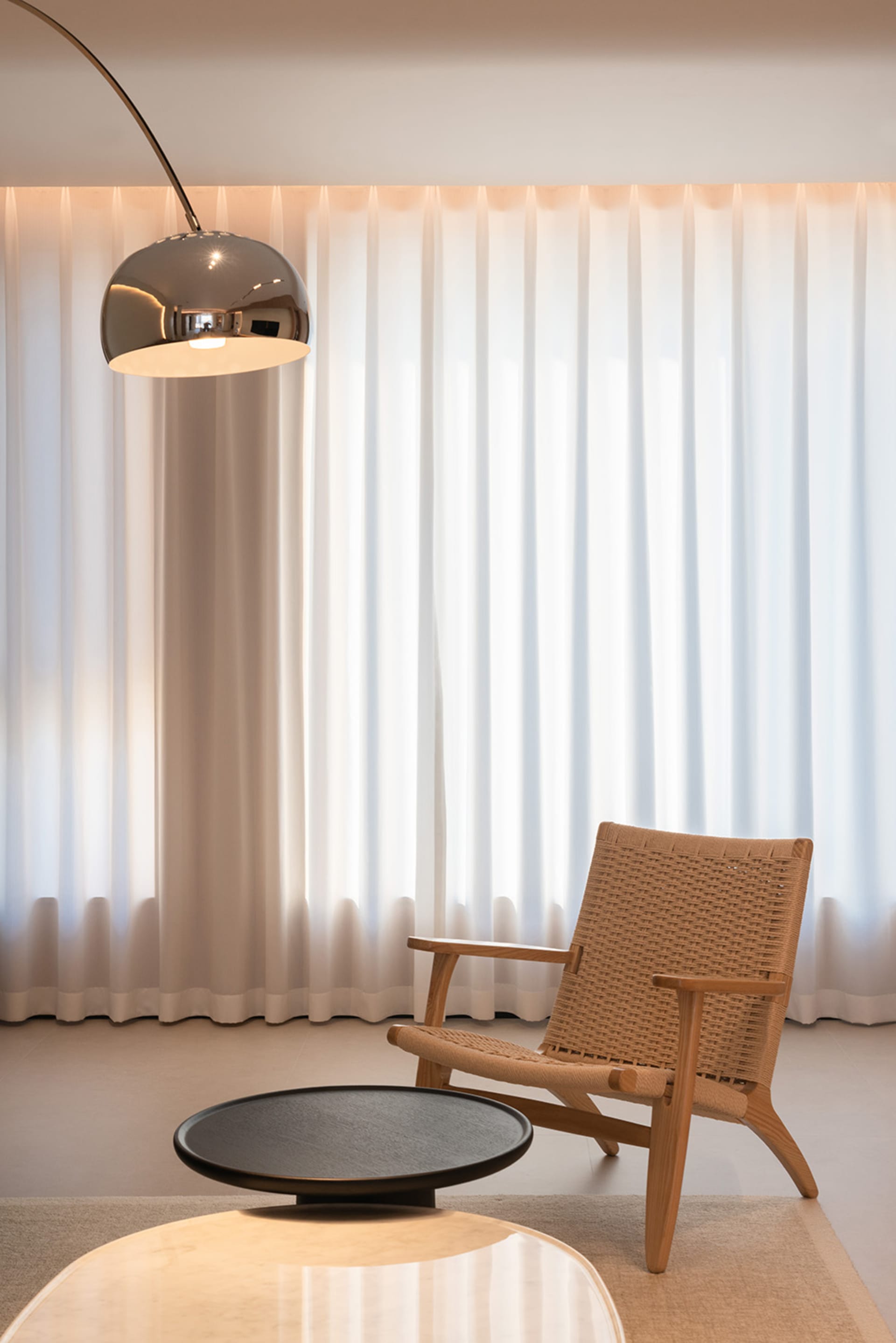Minimalist living room featuring a wooden chair with textile seating, a black round coffee table and sheer curtains.