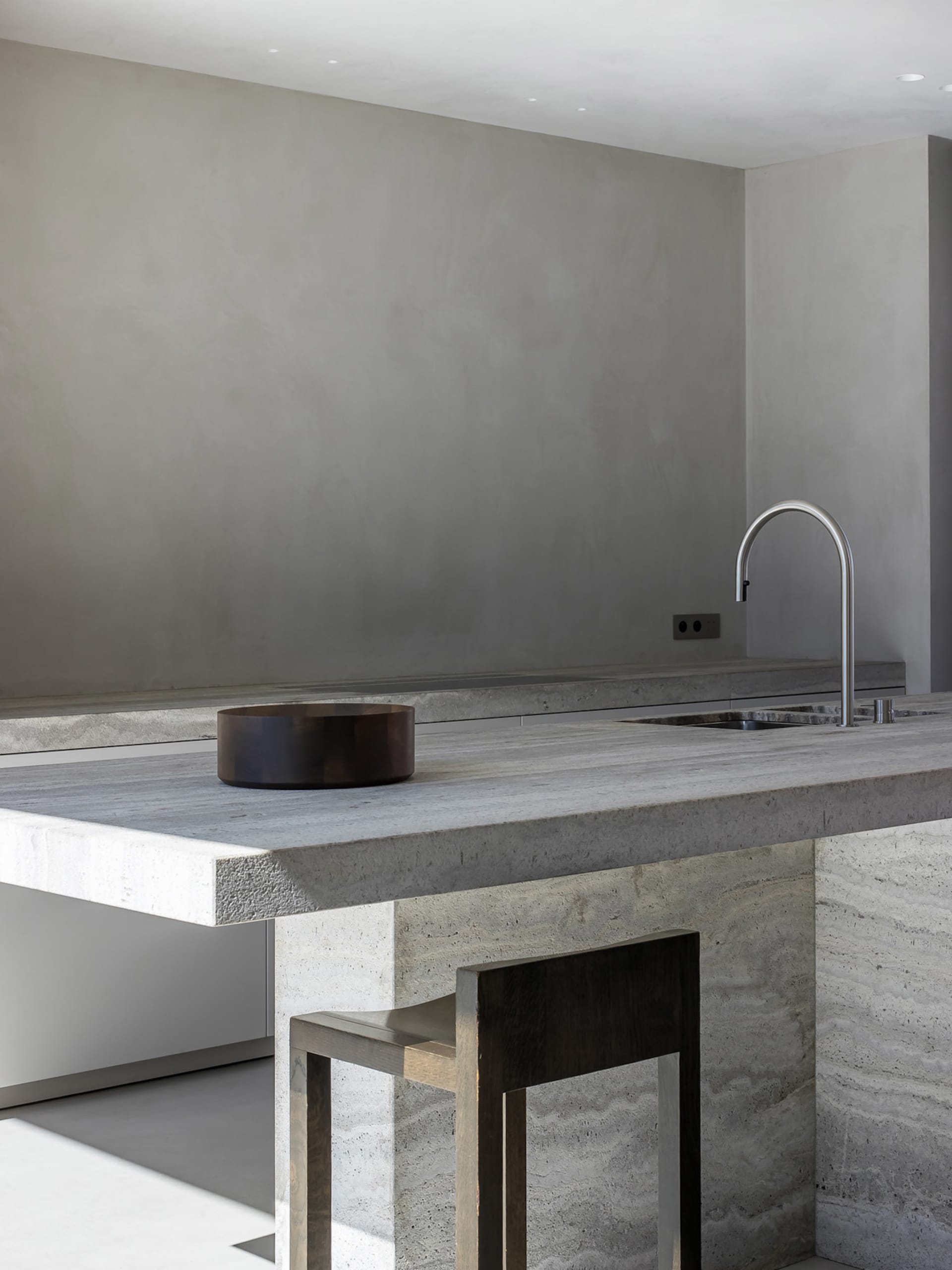 Modern minimalist residential kitchen featuring a concrete countertop with a wooden bowl and minimalist faucet.