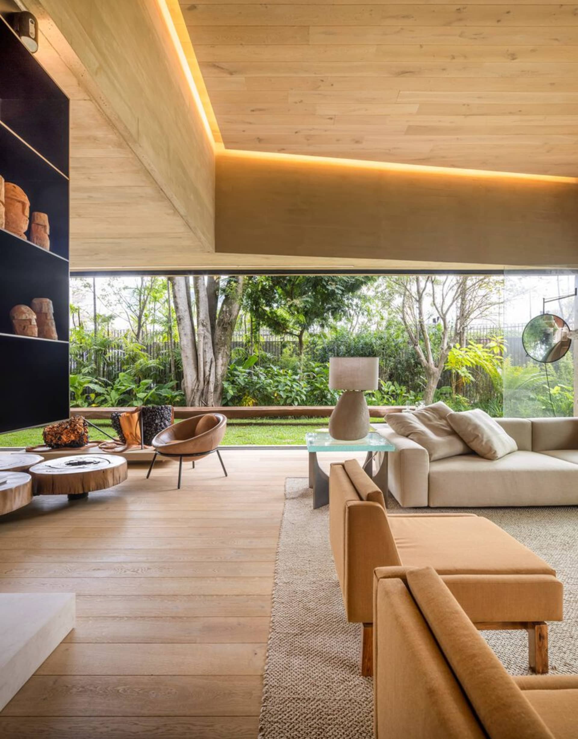 A spacious modern living room with wooden flooring, furniture, and ceiling, featuring a large window overlooking a garden.