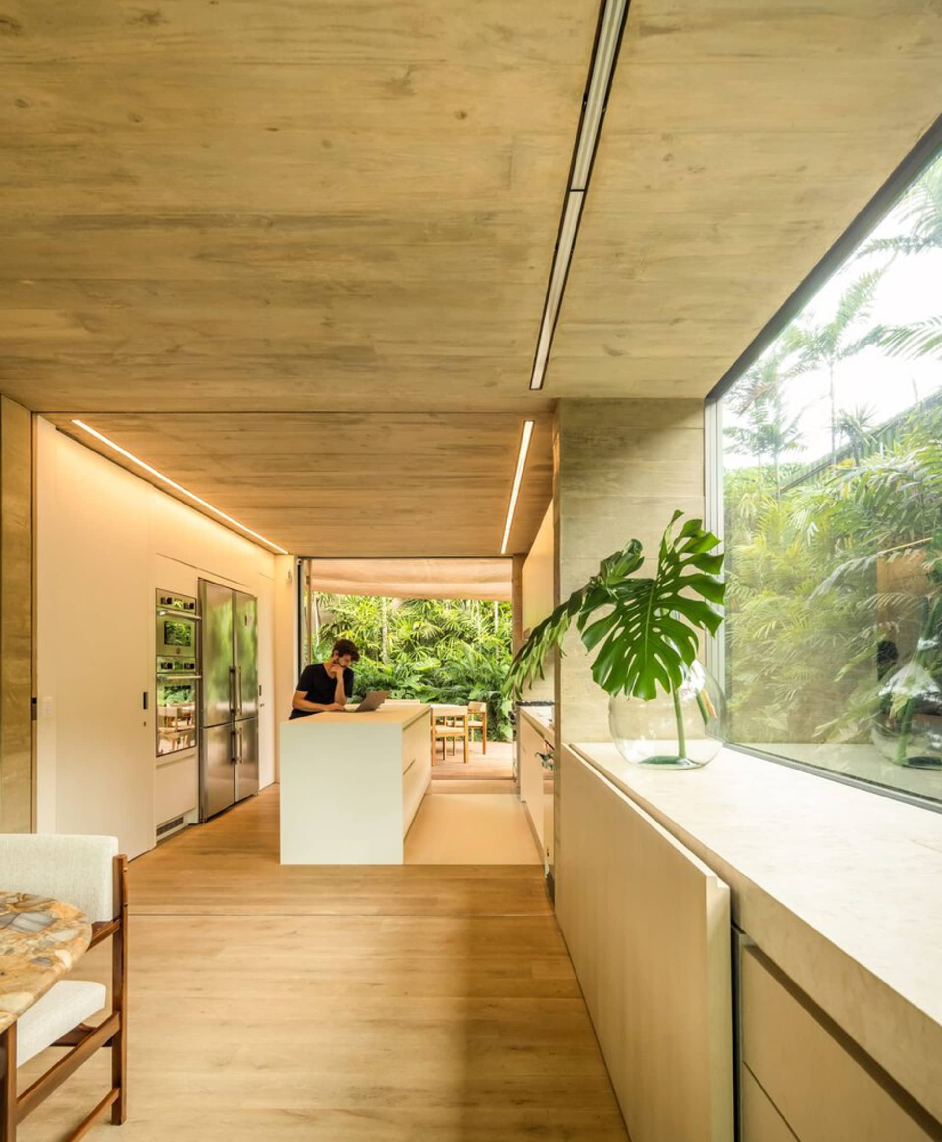 Contemporary residential kitchen featuring minimalist design, concrete finishes, and a large window showcasing lush greenery.