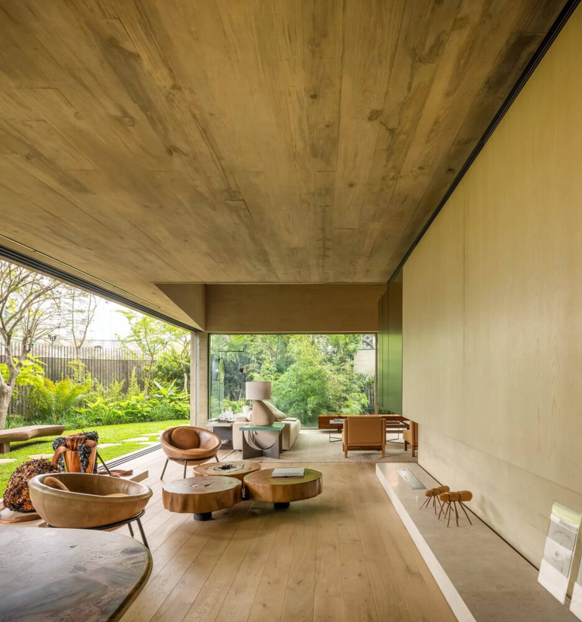 A modern living room with wooden furniture, concrete walls, and a glass door leading to a green outdoor space.