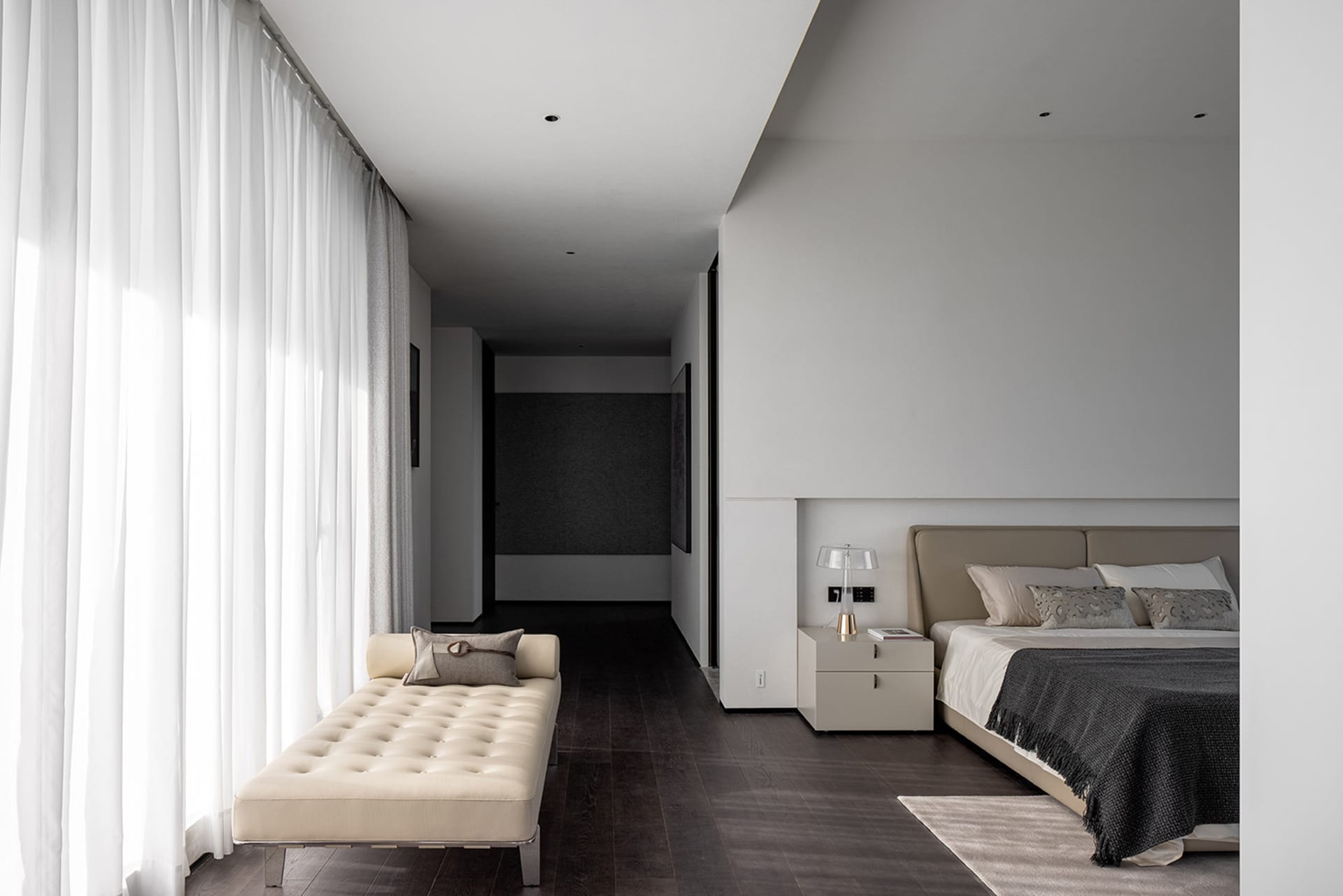 Modern bedroom with neutral decor, featuring a minimalist bed and a beige lounge chair.