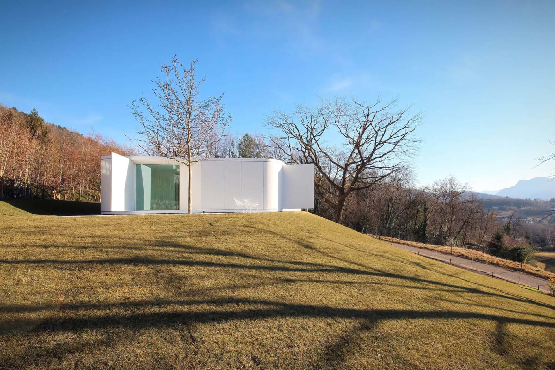 Modern house with white exterior and curved design on a grassy hill