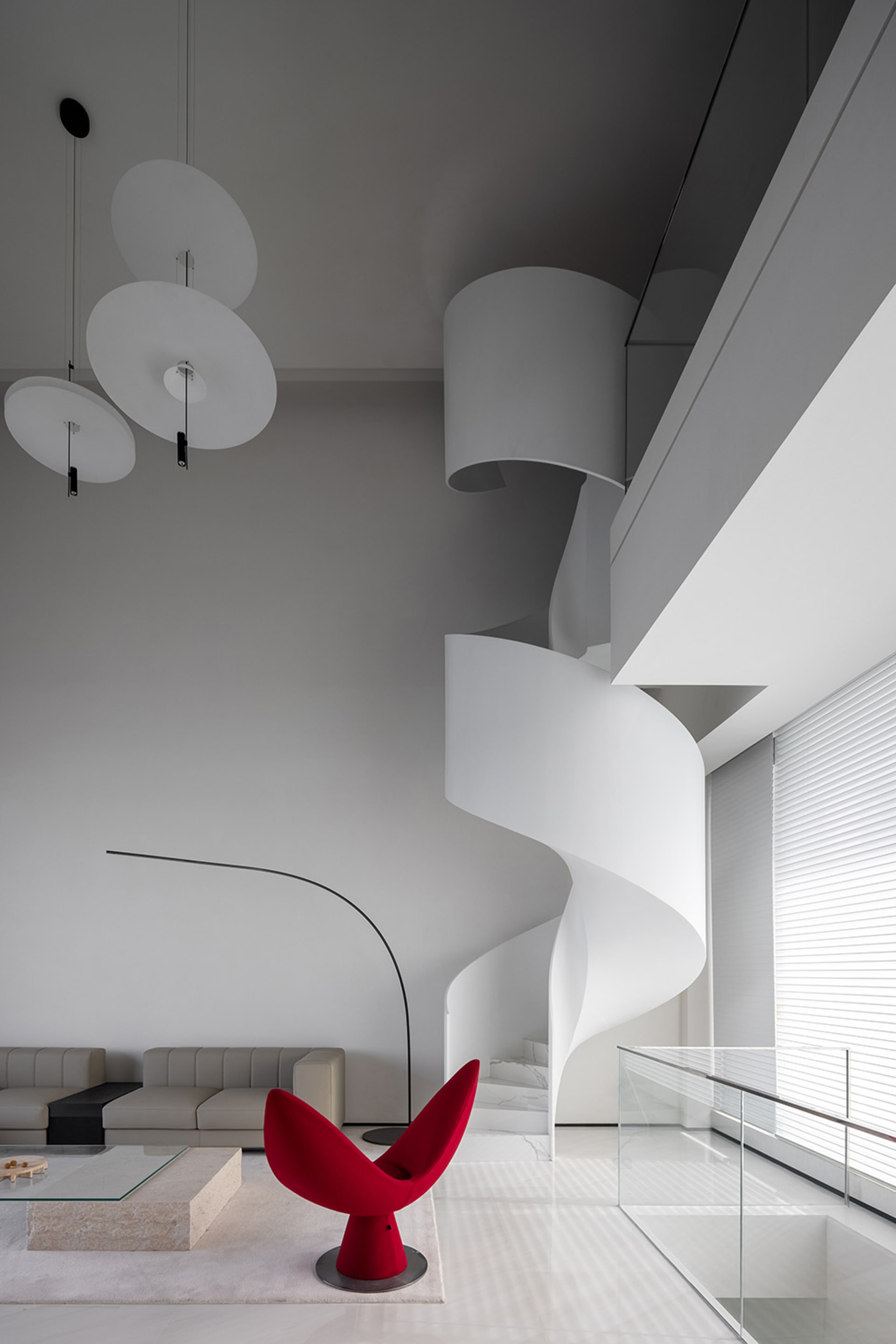 A modern residential interior featuring a minimalist design with a spiral staircase, red chair, and white interior.