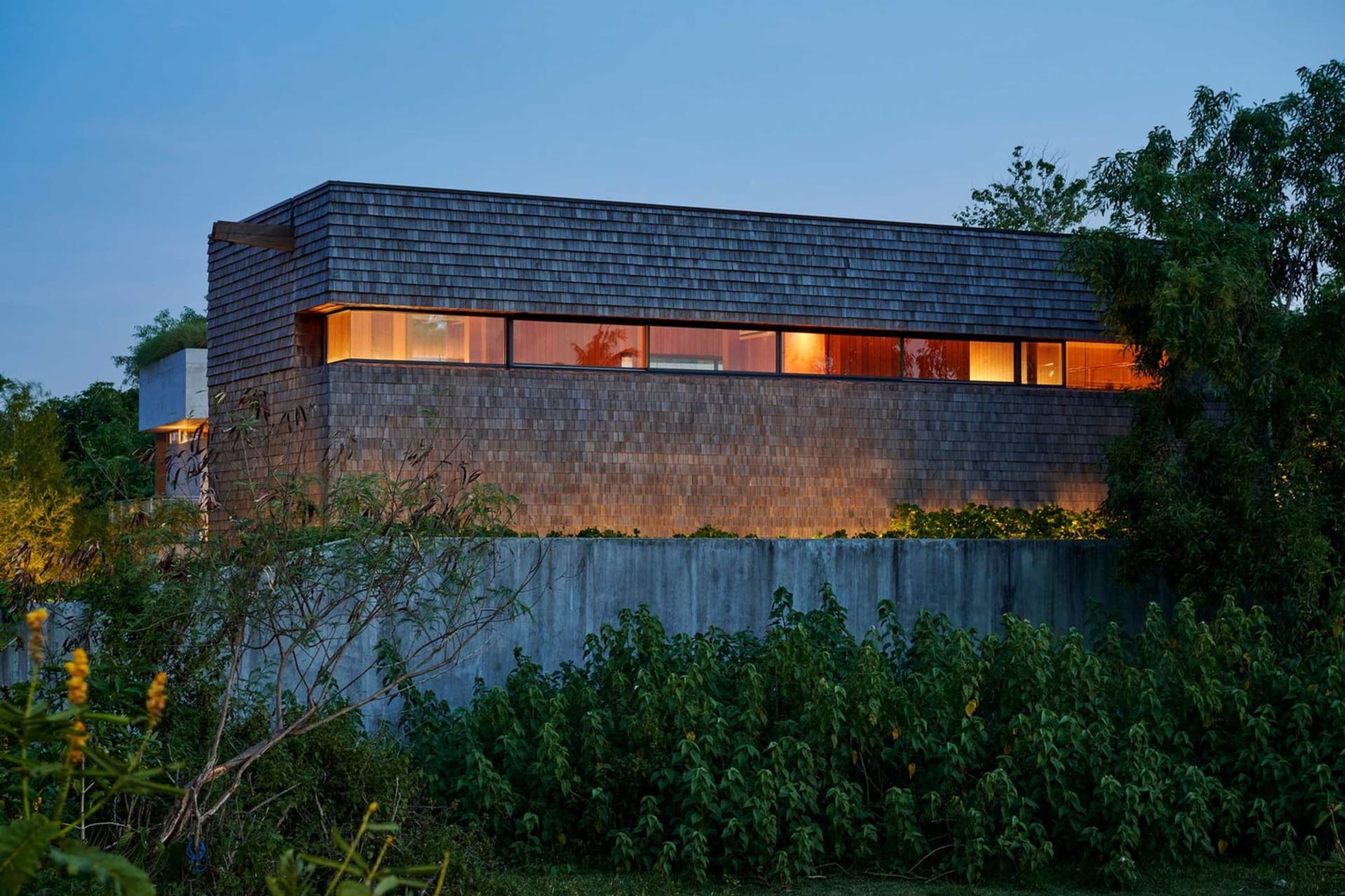 A modern residential house with a wooden exterior at night, illuminated windows.