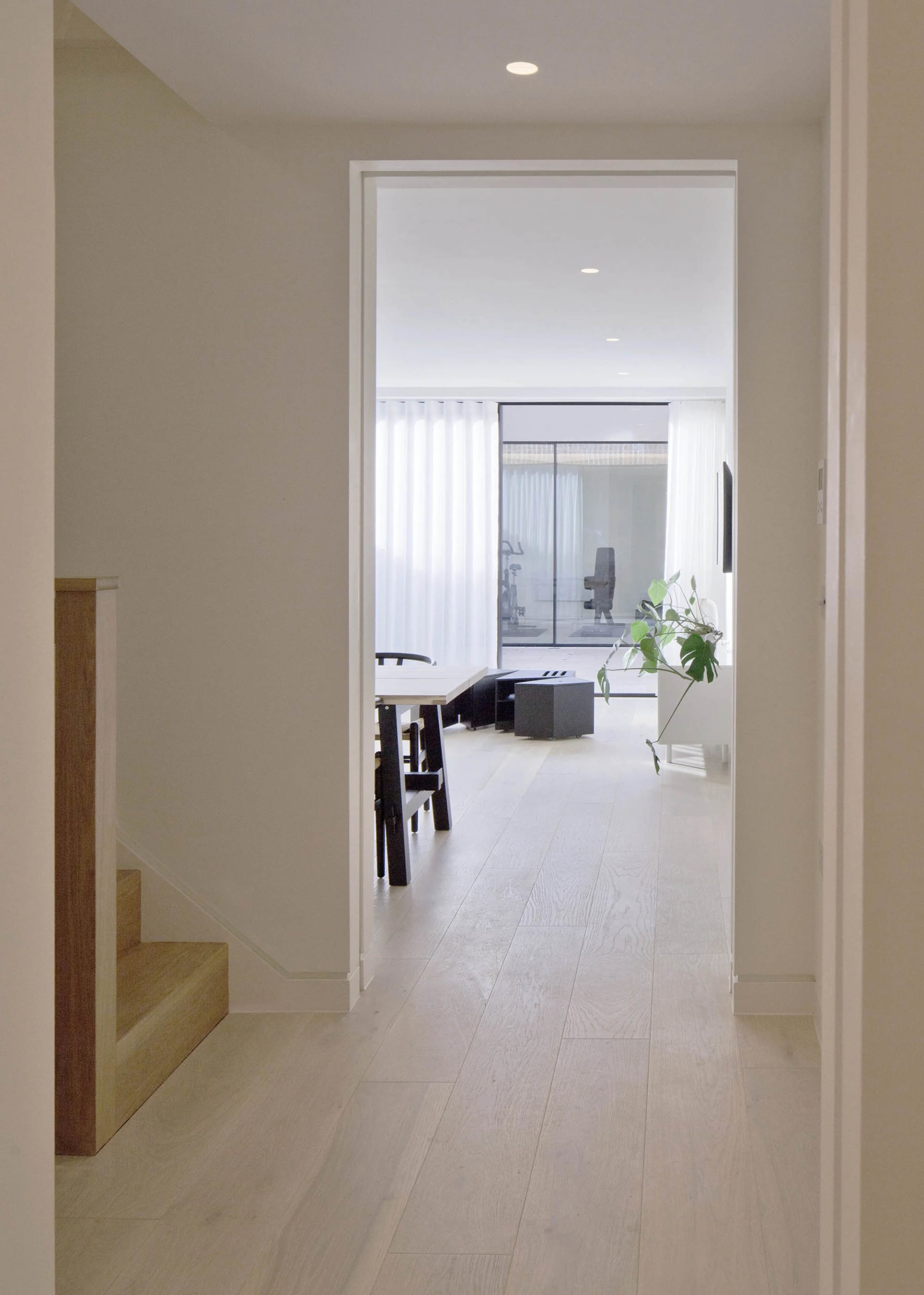 Modern hallway with white wooden flooring, glass doors, and minimal decor.