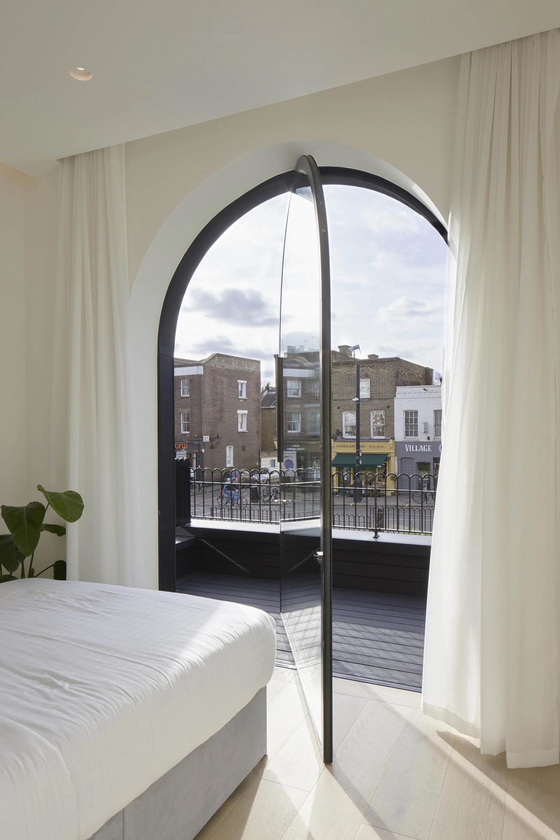 A modern bedroom features a glass window overlooking a residential area.