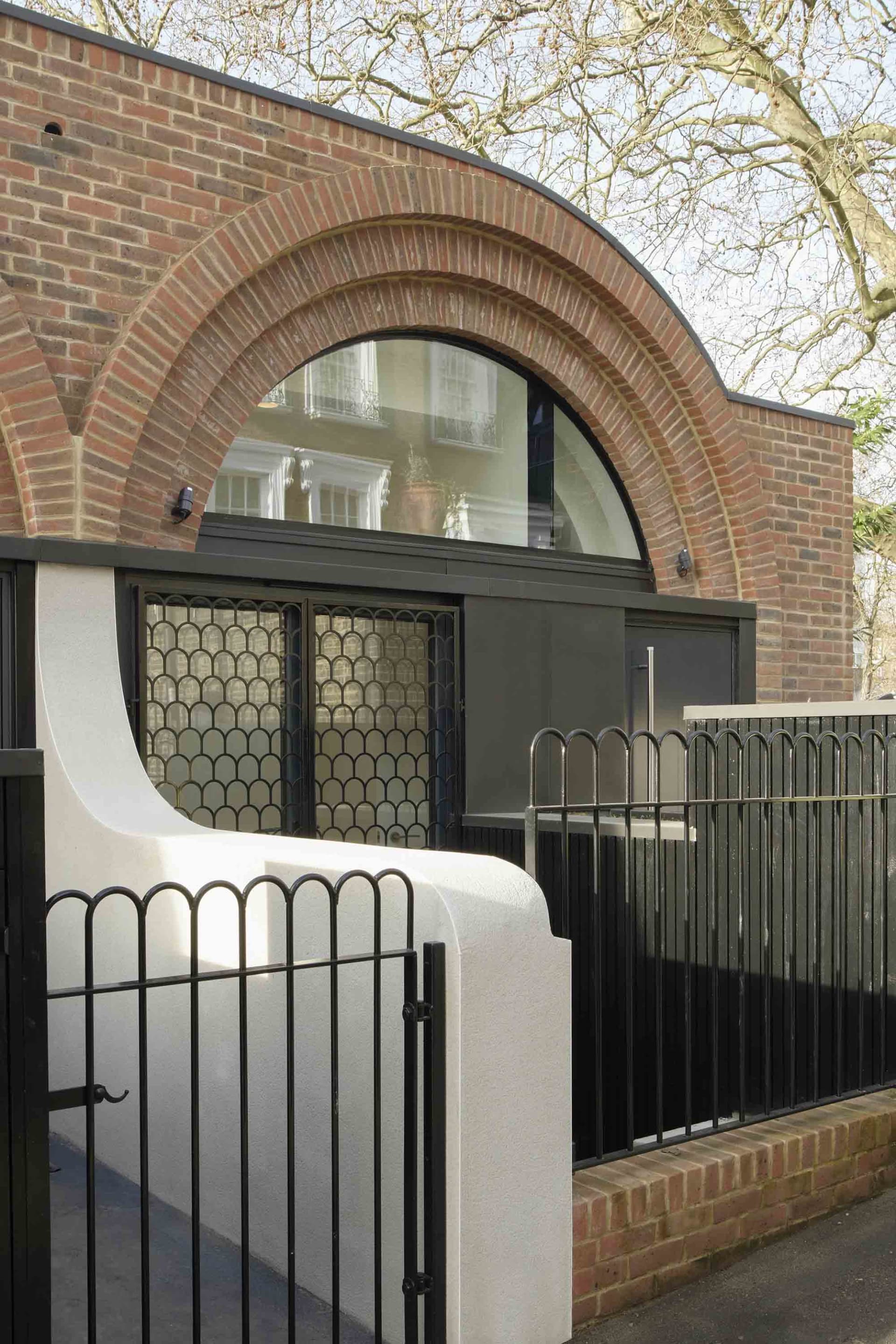 A modern building with an arched brick facade and a black metal fence.