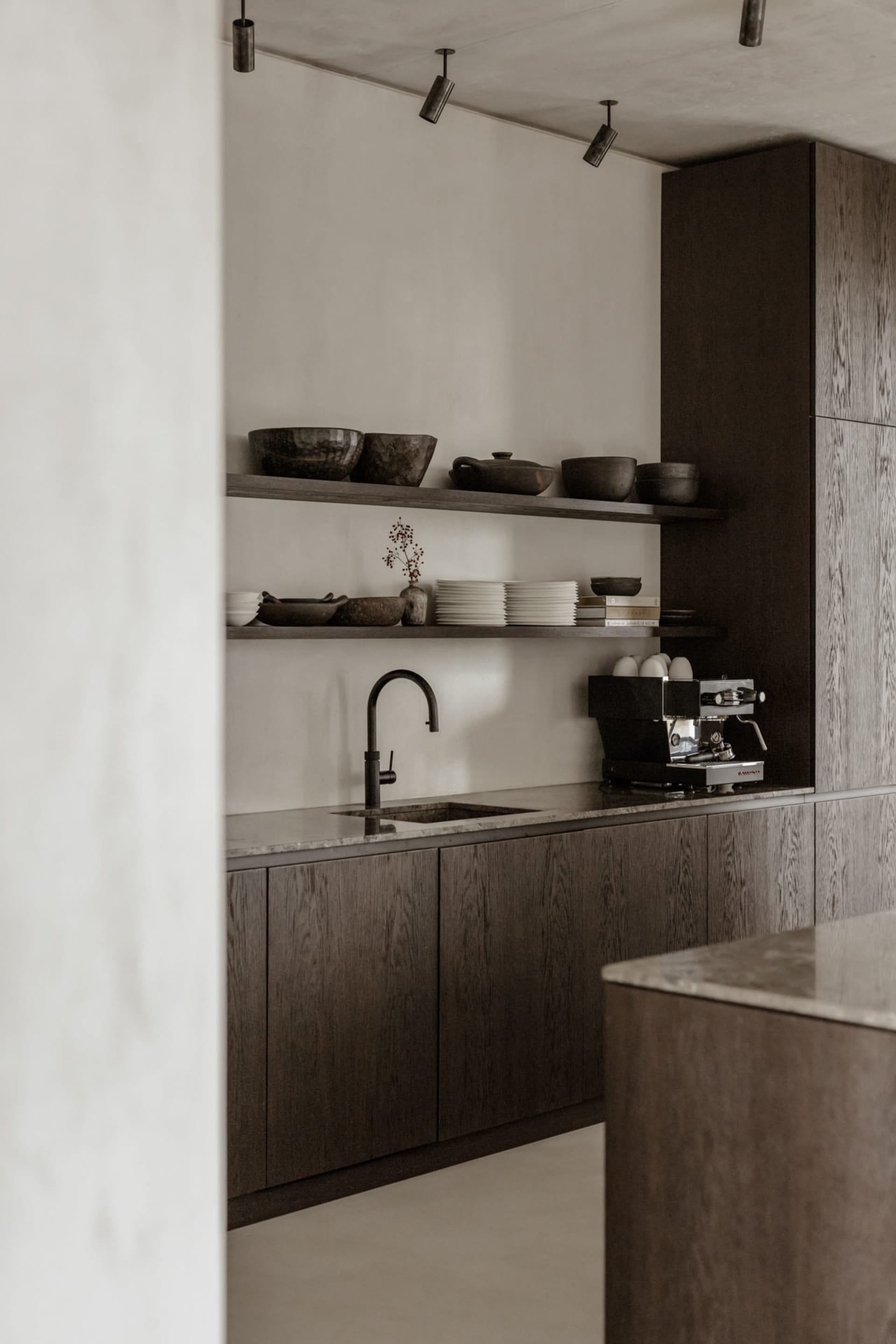 Minimalist kitchen with dark wood cabinets, marble countertop, and black faucet.