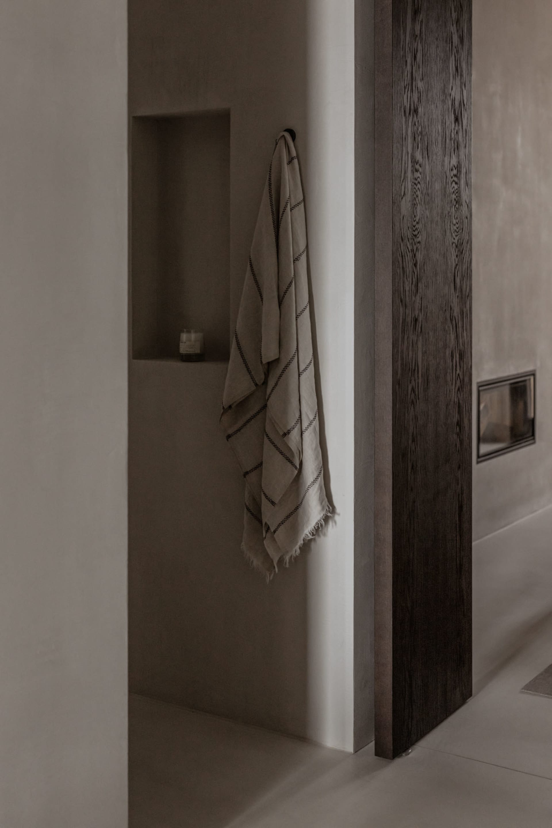 A minimalist bathroom with concrete walls, a towel hanging on the wall, and a built-in shelf.