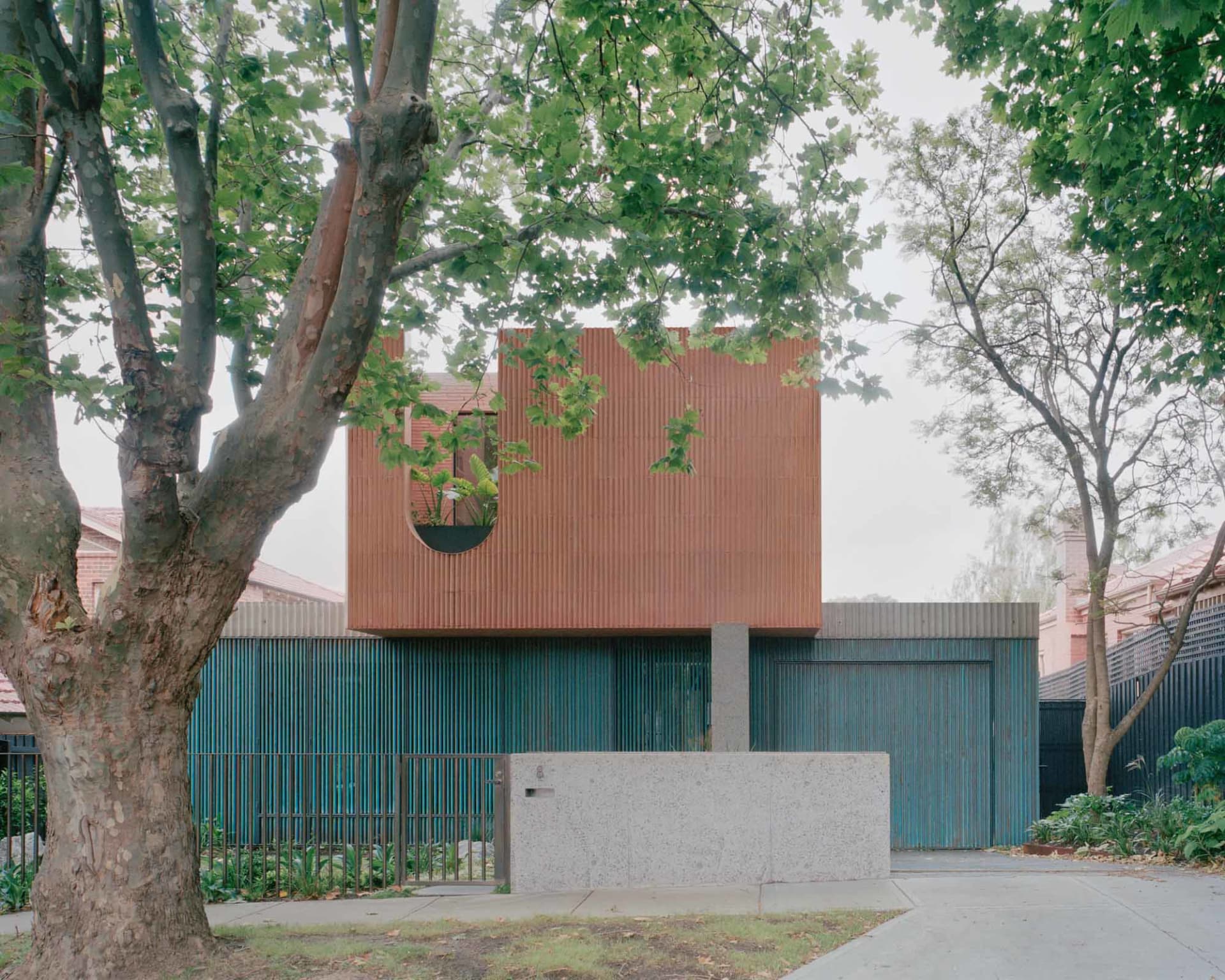 現代住宅採用金屬外牆與綠意植栽,坐落於都市環境,周圍環繞樹木。