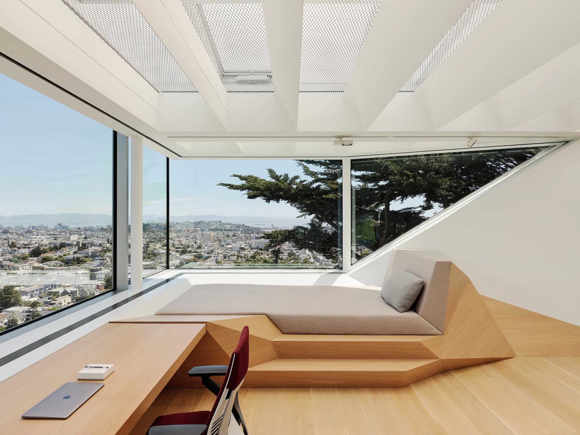A modern office space featuring large glass windows with a view of the city, a wooden desk, and a comfortable seating area.