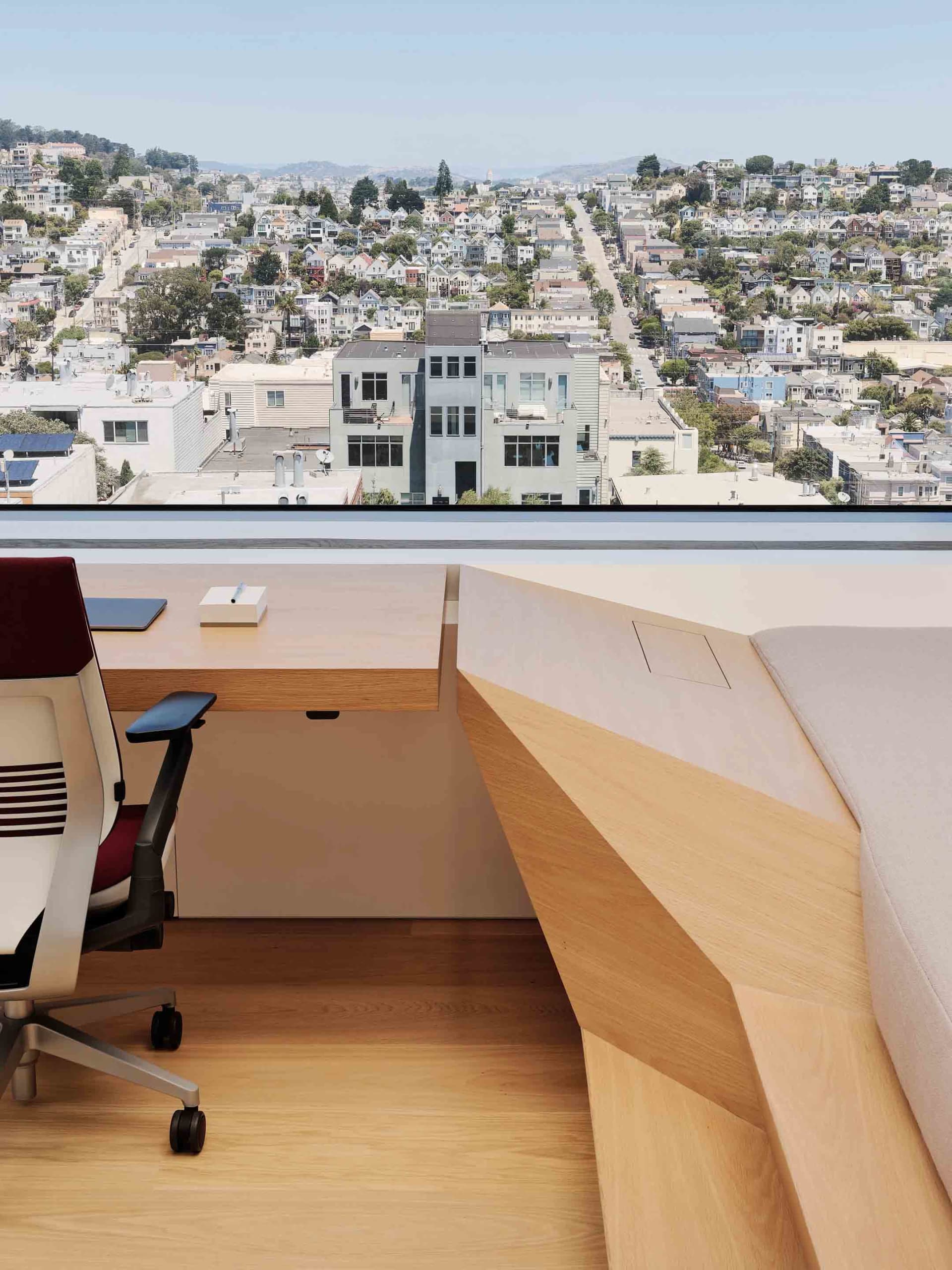 A modern office with a view of a cityscape, featuring a wooden desk and comfortable seating.