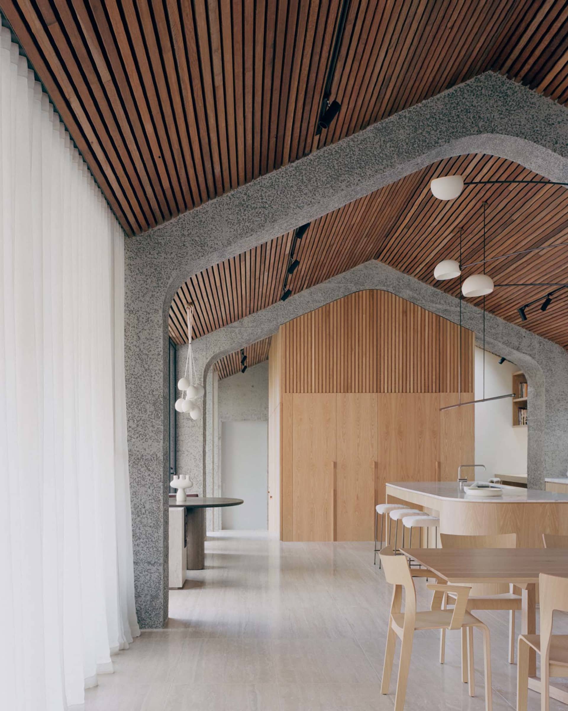 Modern interior space with wooden slat ceiling and walls, concrete structural elements, and minimalist furniture.