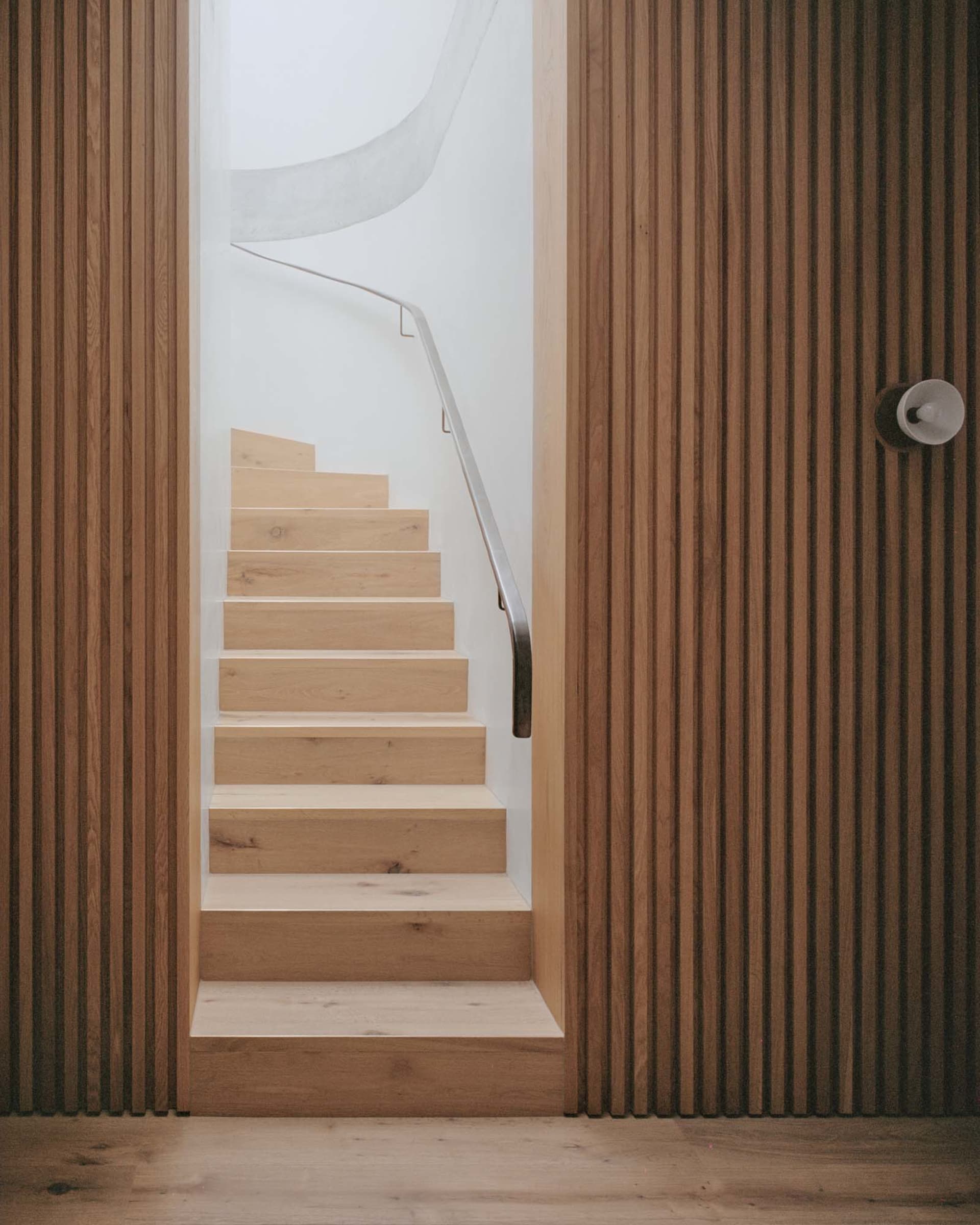 A minimalist staircase with wood steps and a metal railing.