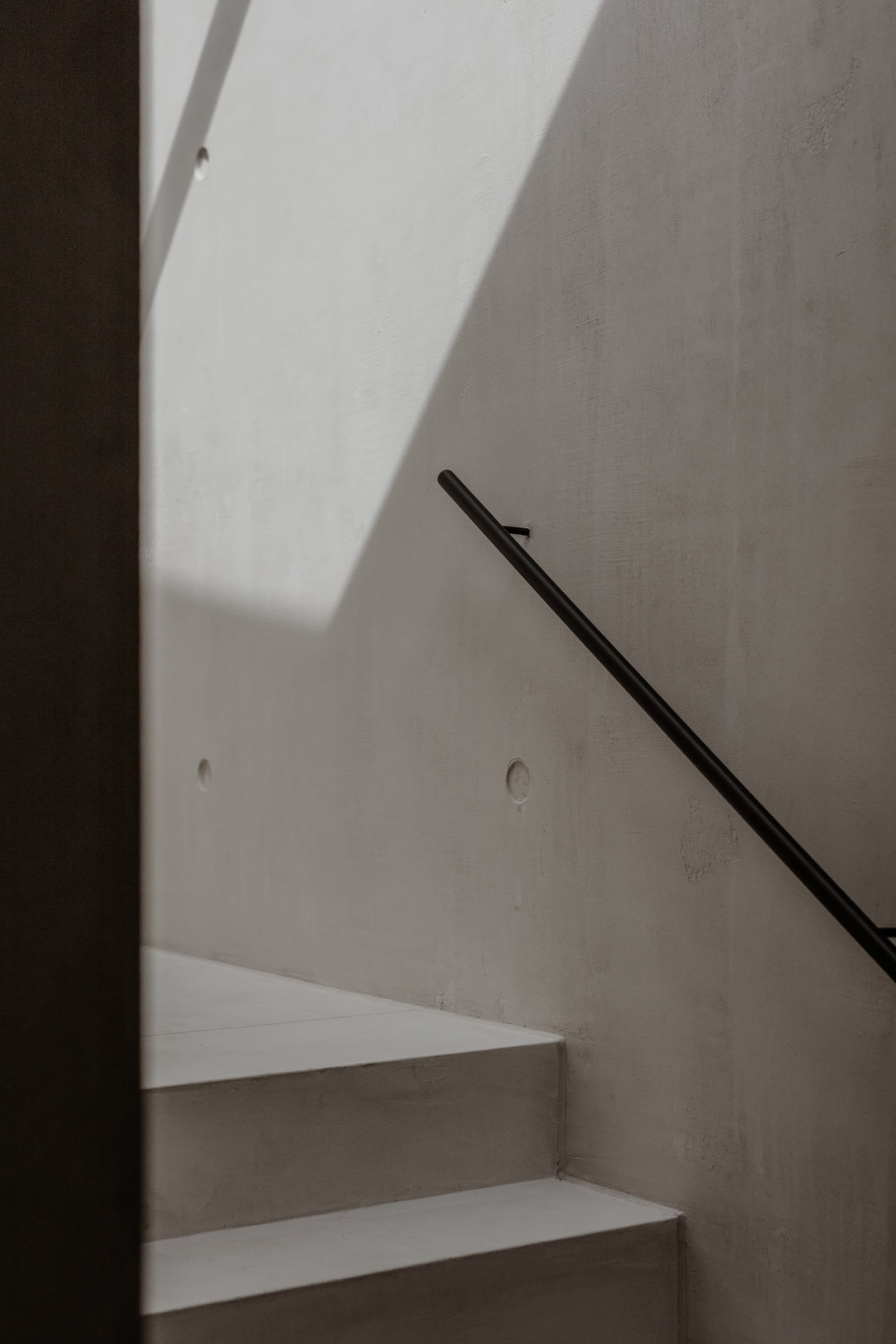 A minimalist staircase with a concrete wall and a black handrail.