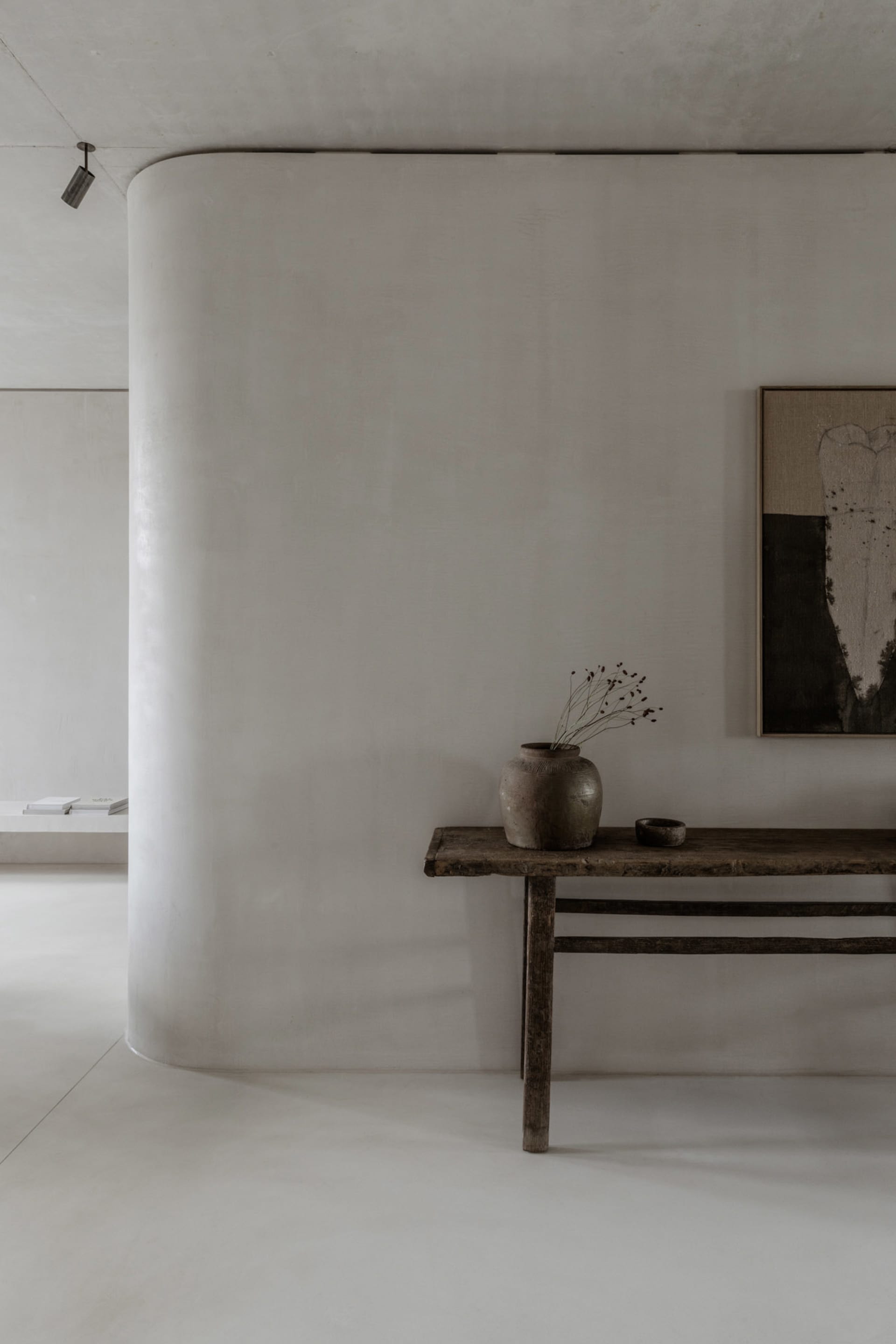 A simple, minimalist living room console table adorned with a vase of dried flowers and a bowl, against a smooth, white wall