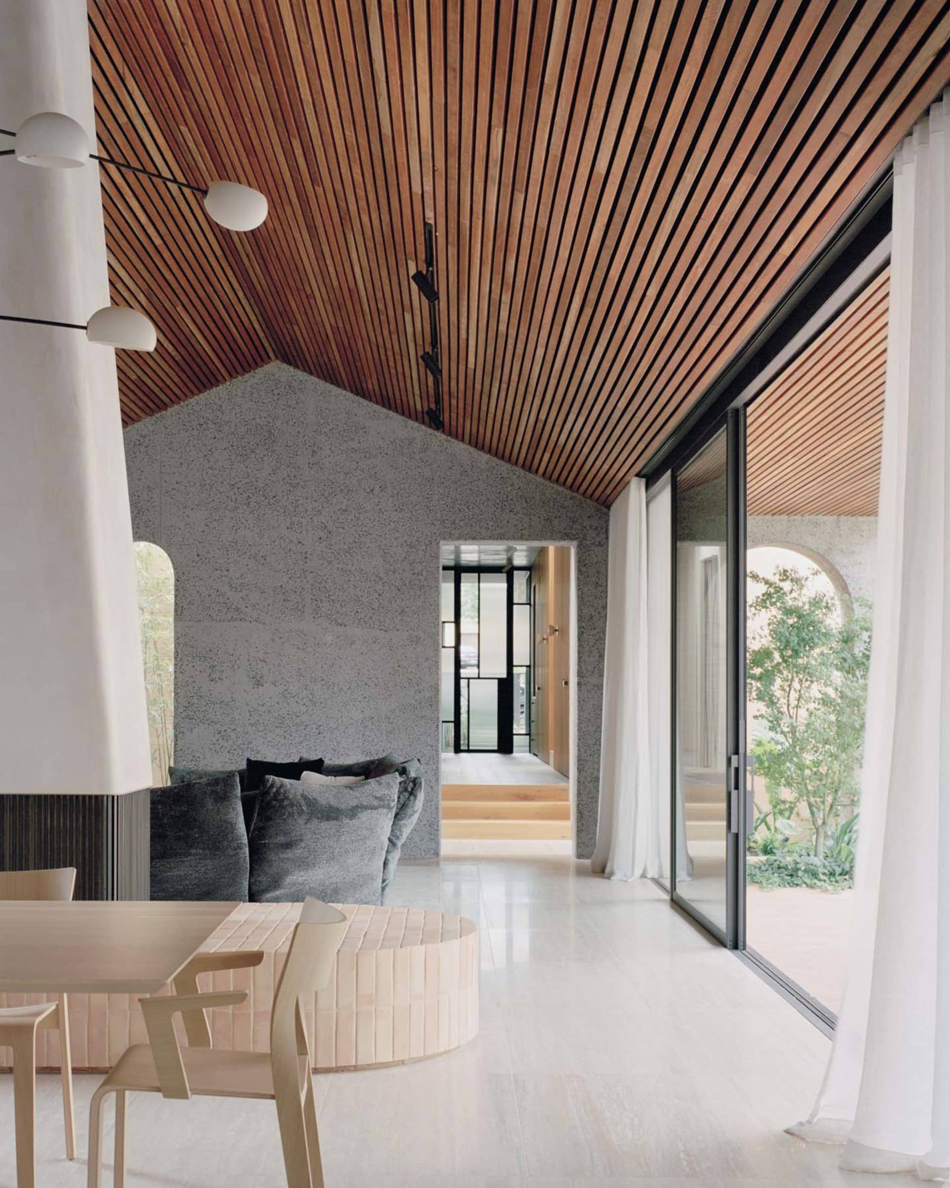 Modern living room with wooden ceiling, concrete walls, and large glass doors.