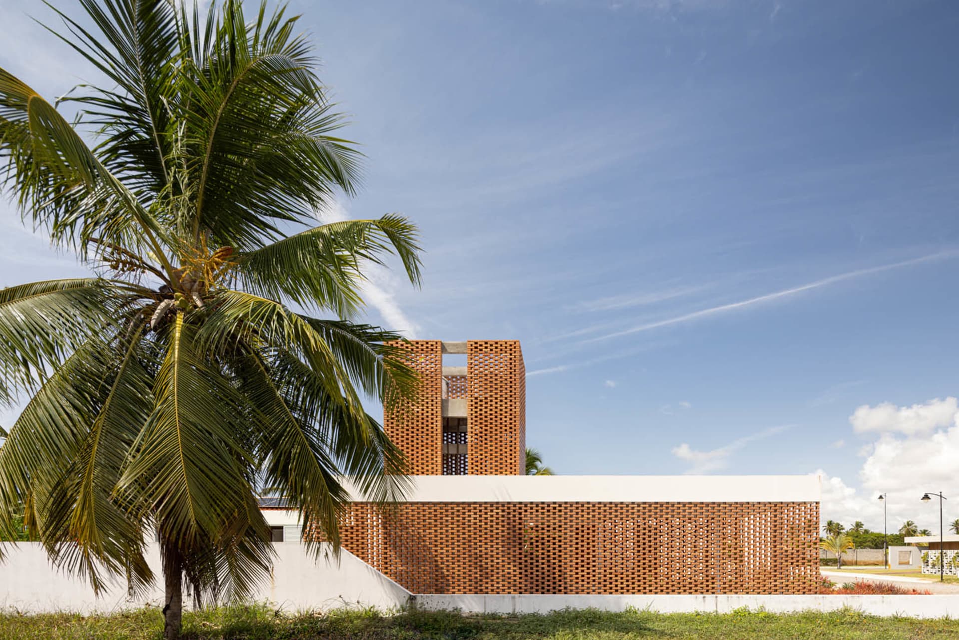A modern brick building with a palm tree in the foreground against a blue sky.