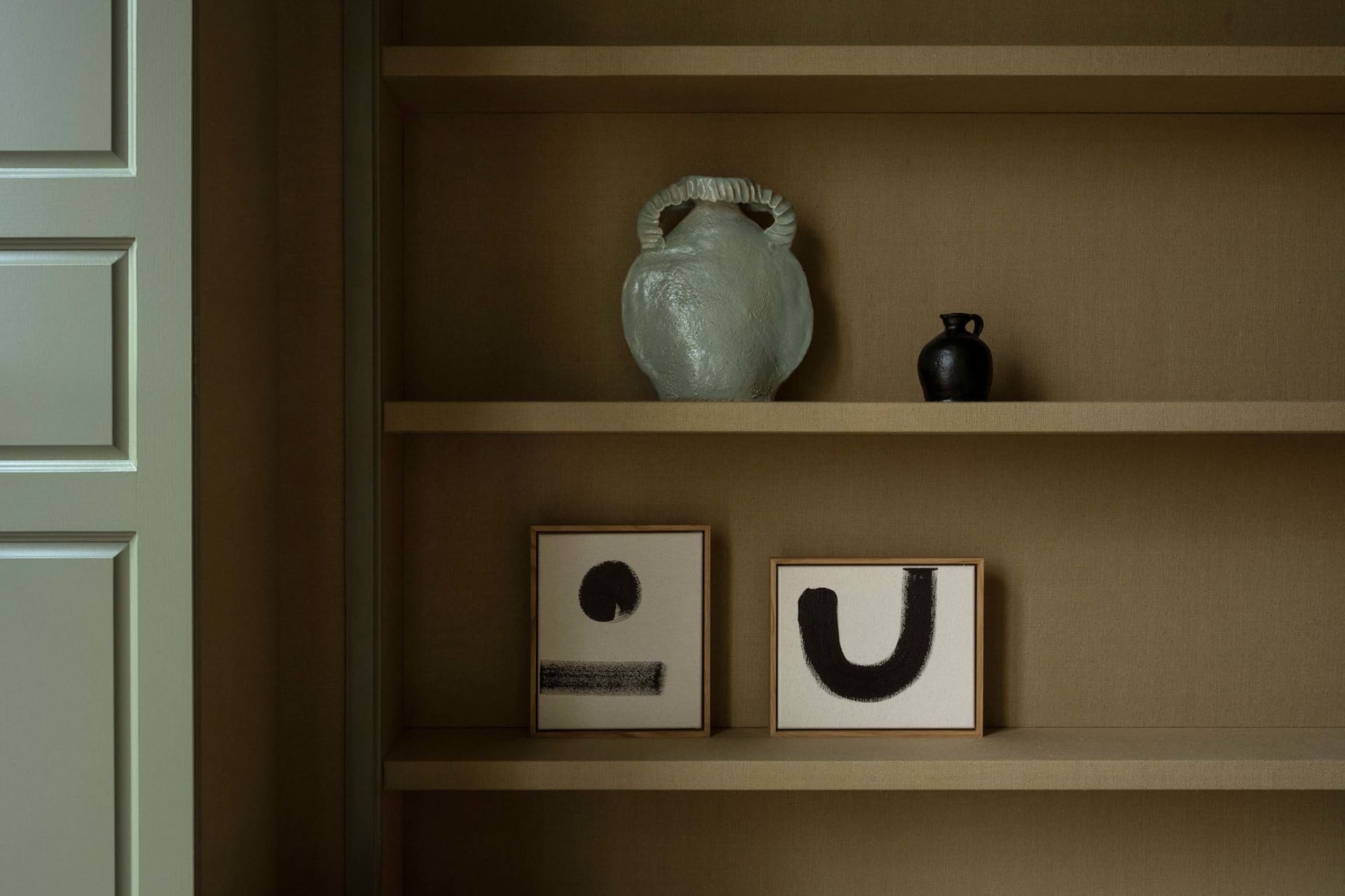 Modern interior design featuring a ceramic vase and abstract paintings on shelves.