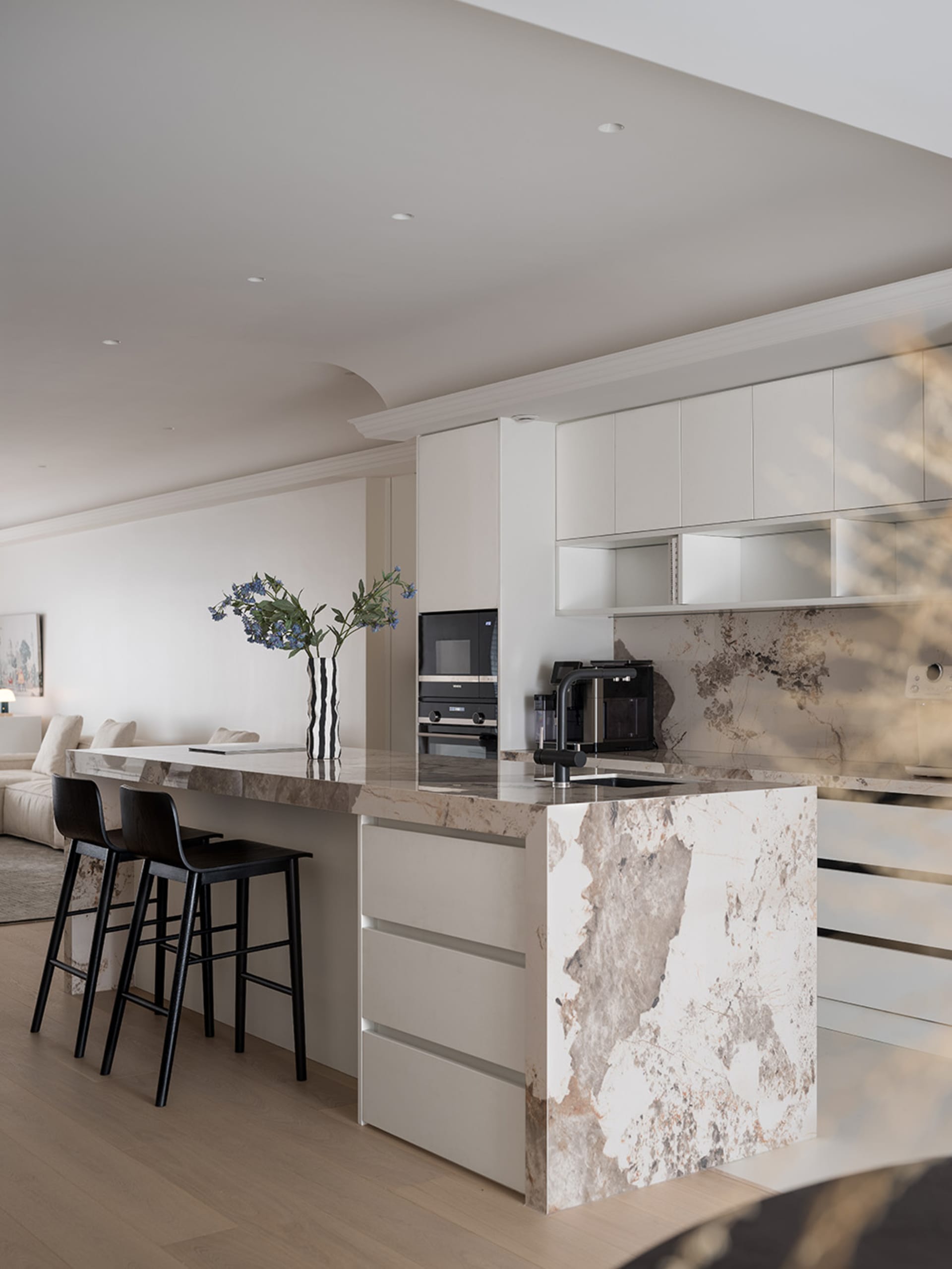 A modern kitchen with a marble countertop and black stools.