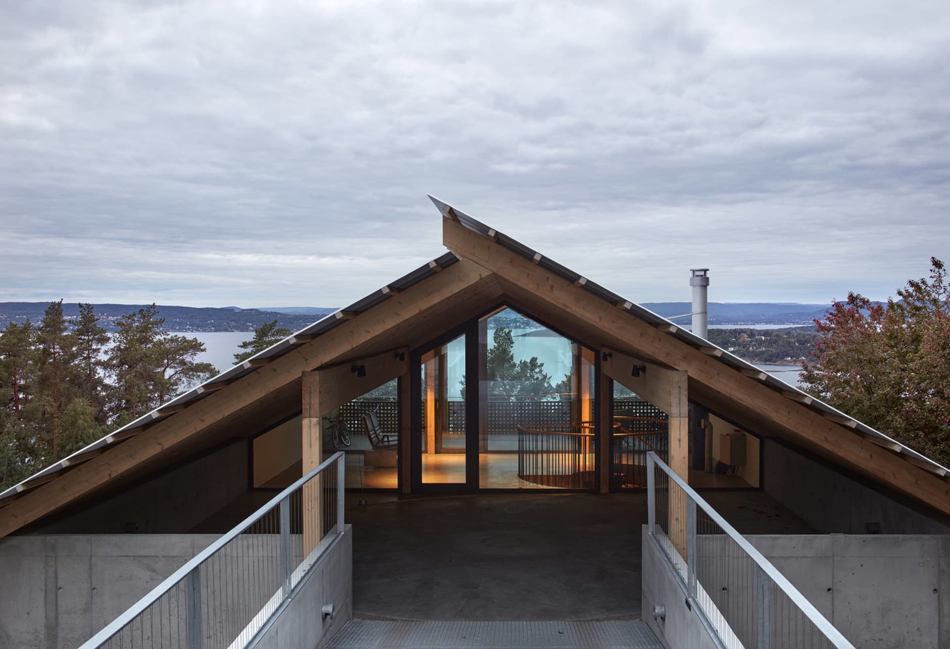 A modern architectural structure featuring a wooden roofline with large windows overlooking a scenic landscape.