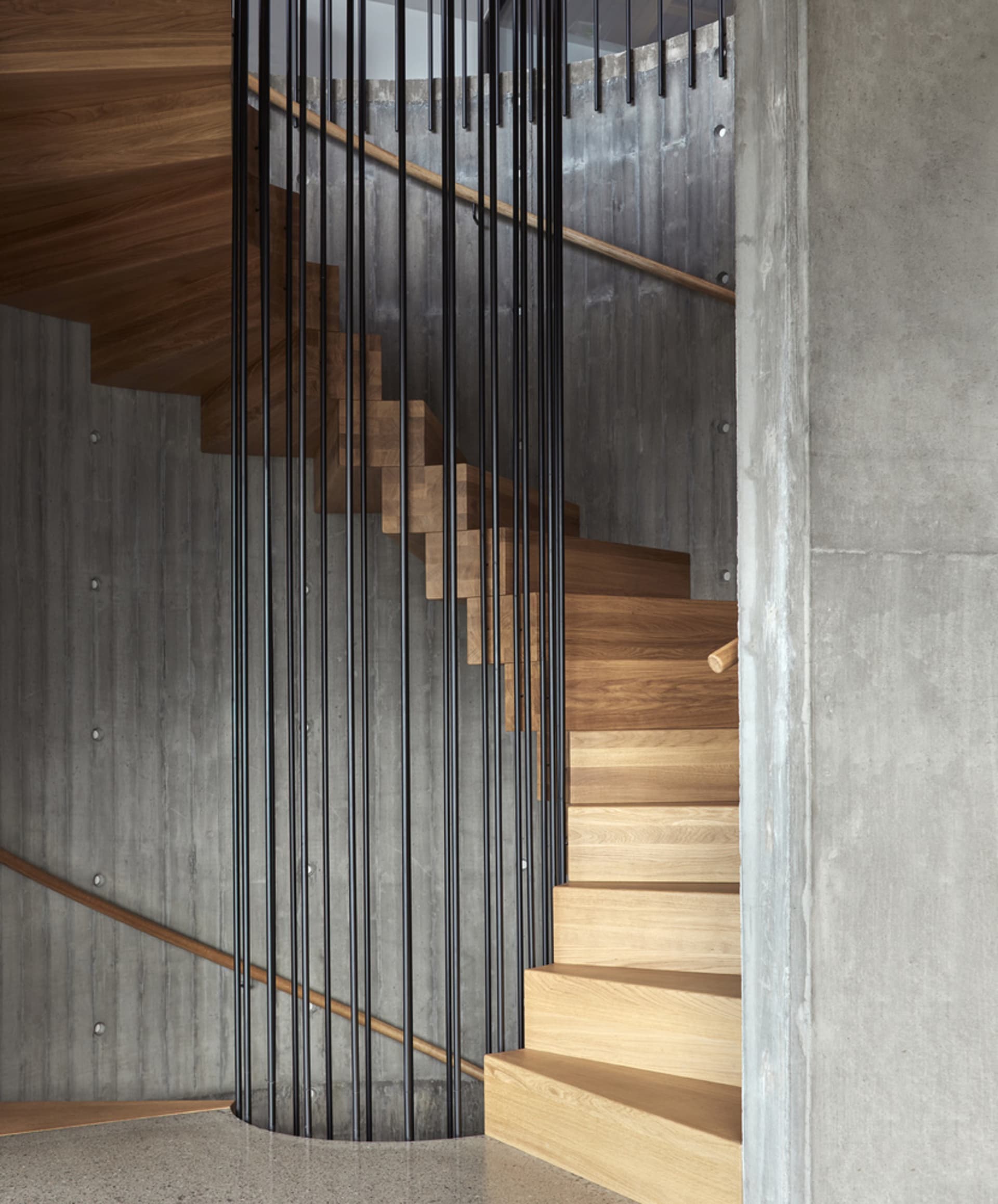 Circular staircase with wooden steps and black metal railings, surrounded by concrete walls.
