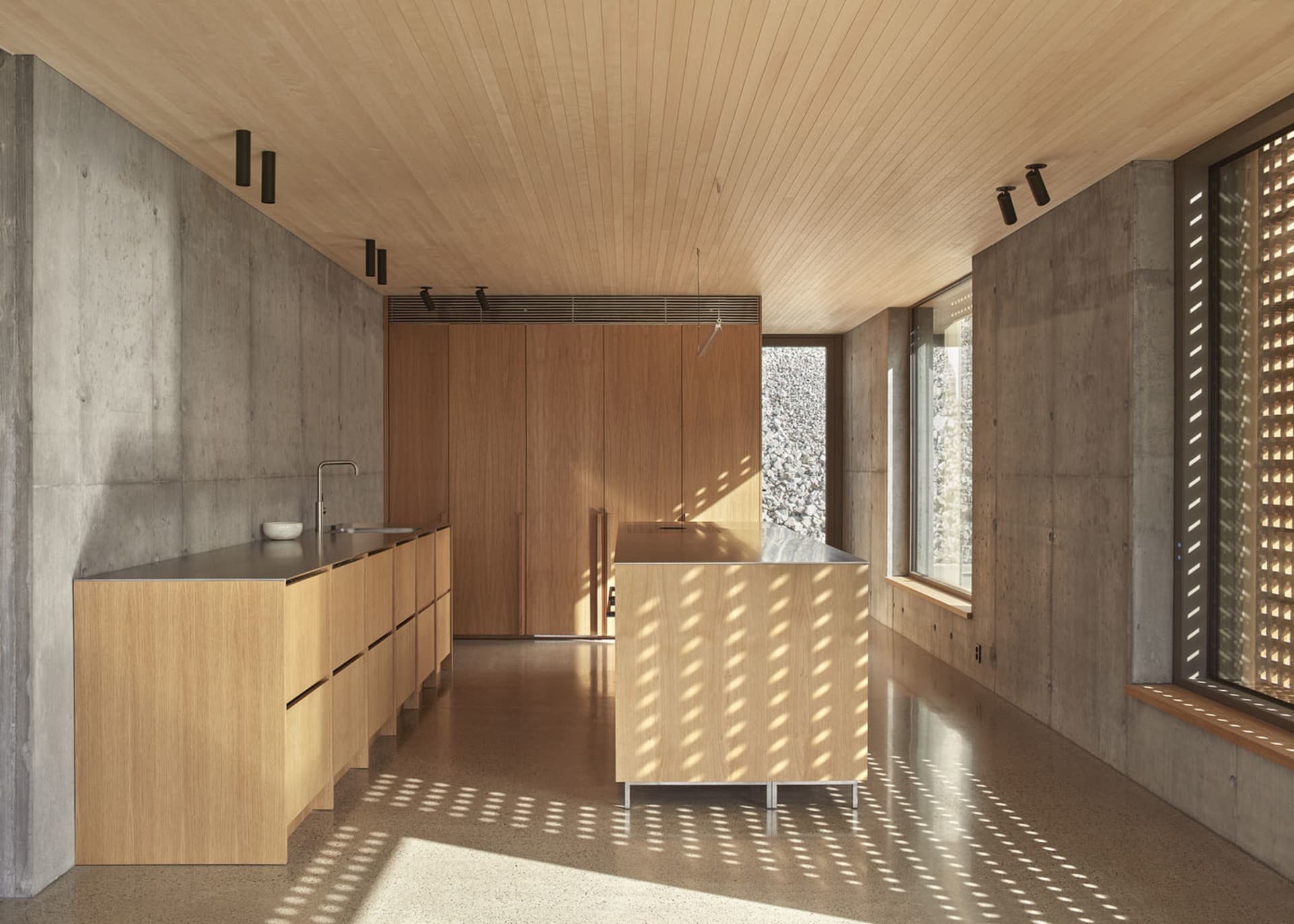 A modern kitchen with wooden cabinets and flooring, featuring a small island with a counter.