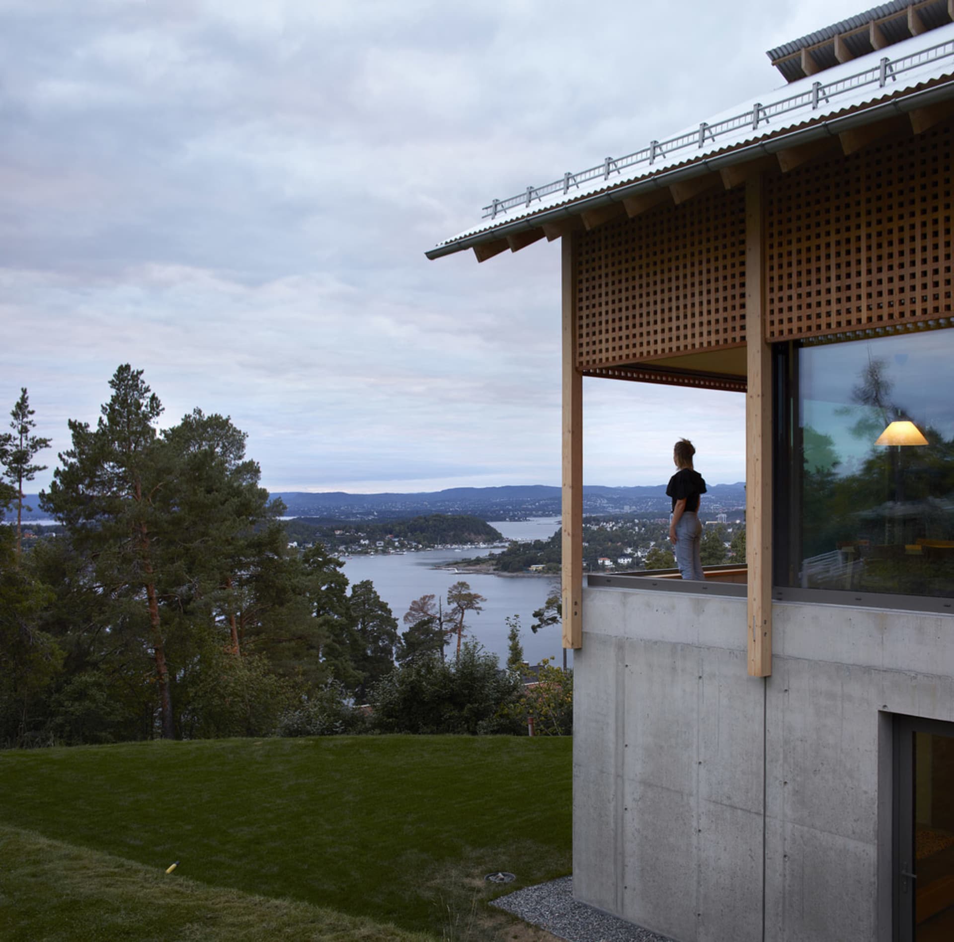 Modern minimalist residential exterior with concrete and wood features overlooking a scenic body of water.