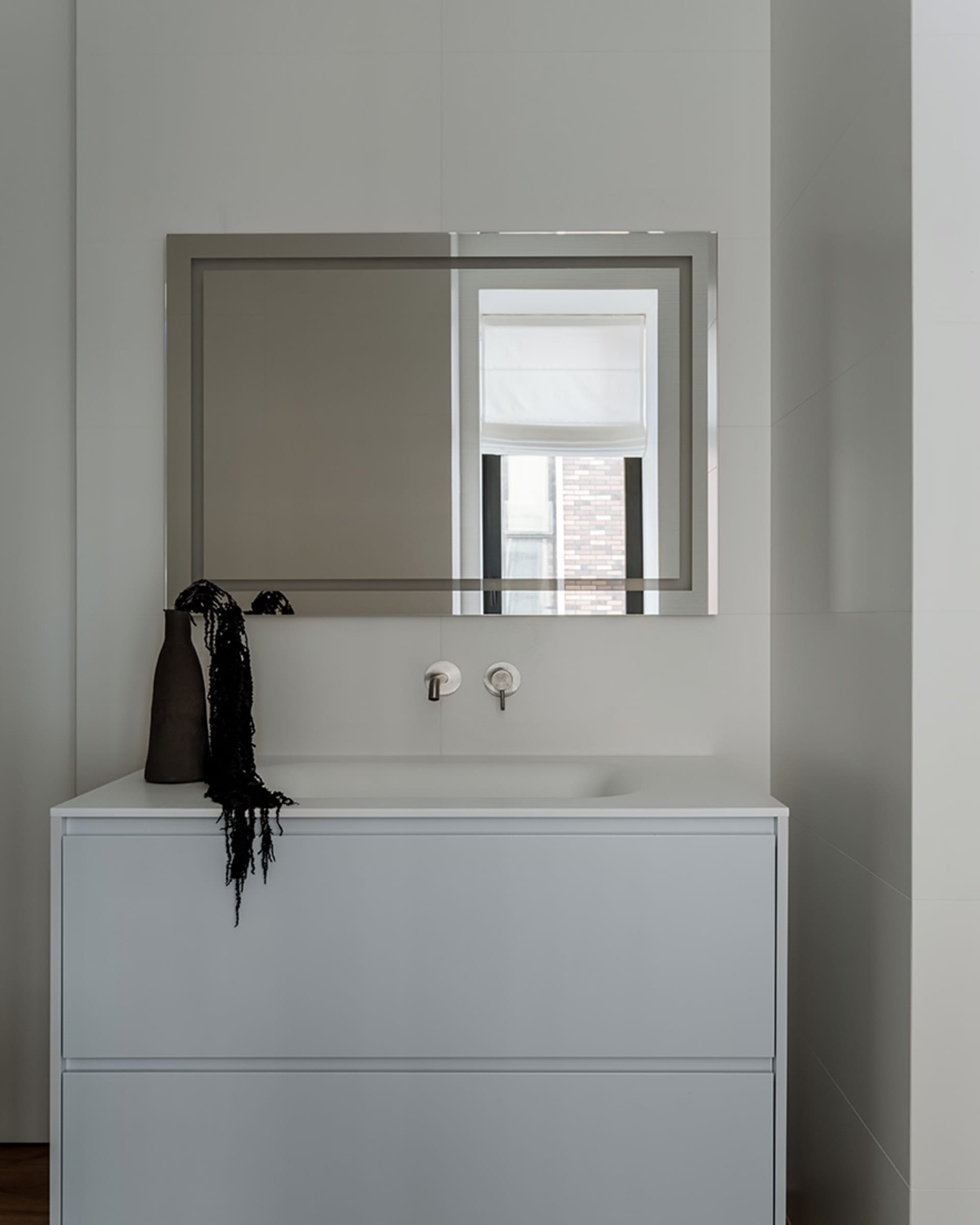Minimalist bathroom with a white ceramic sink, glass wall, and metal fixtures.