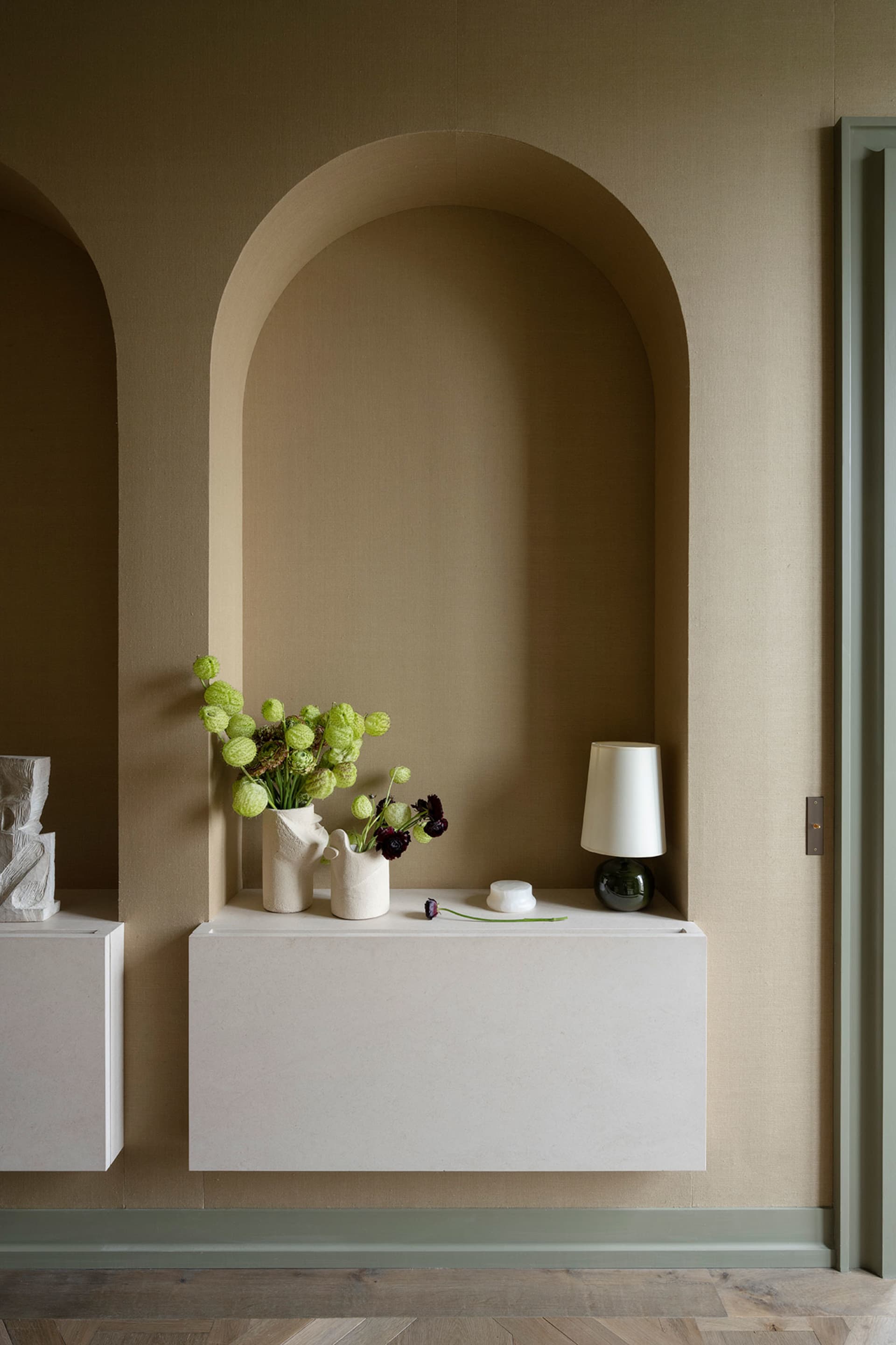 A modern residential entryway featuring a concrete floating shelf with a lamp and flowers.