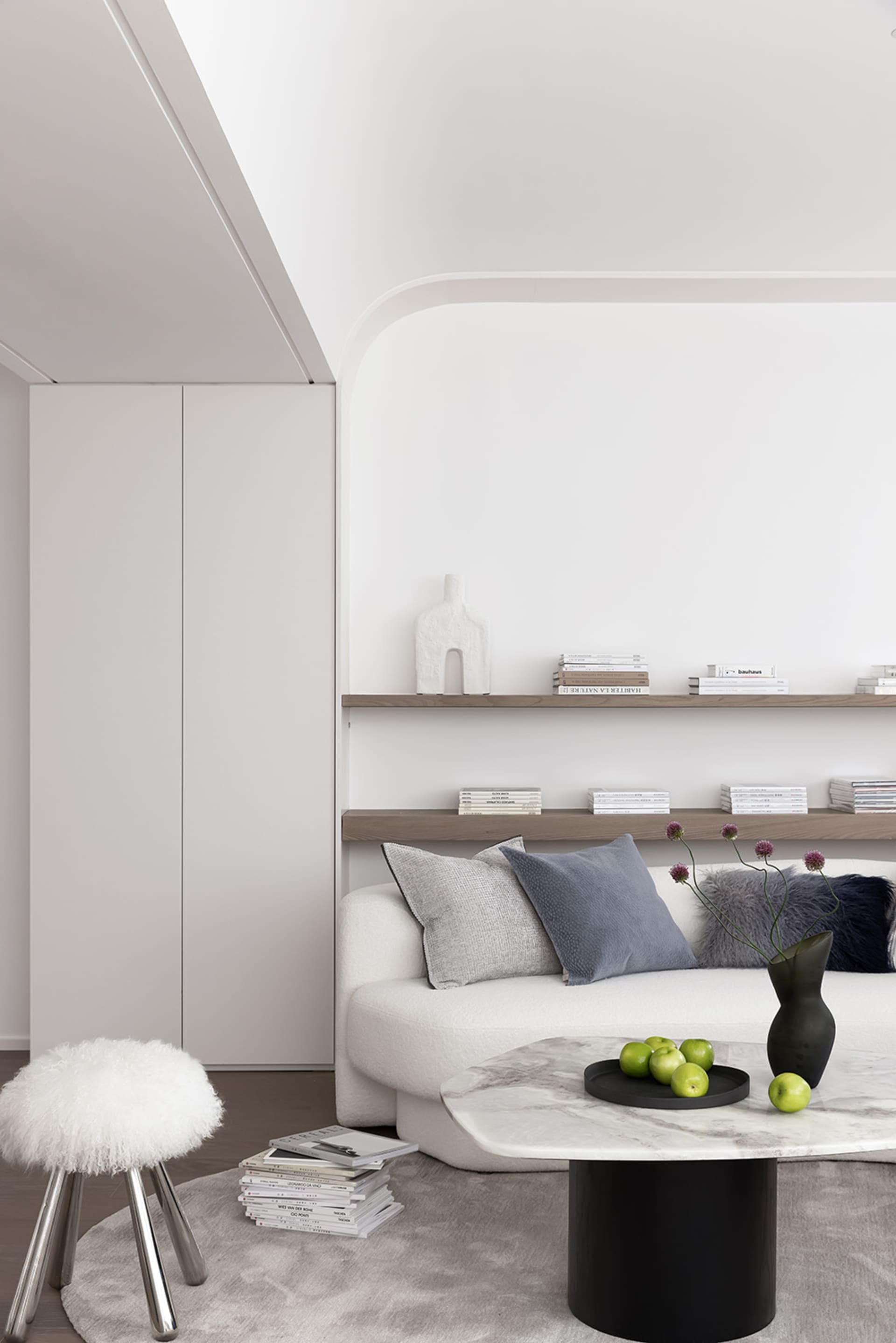 A modern, minimalist living room with a white sofa, wooden shelves, and a marble coffee table.