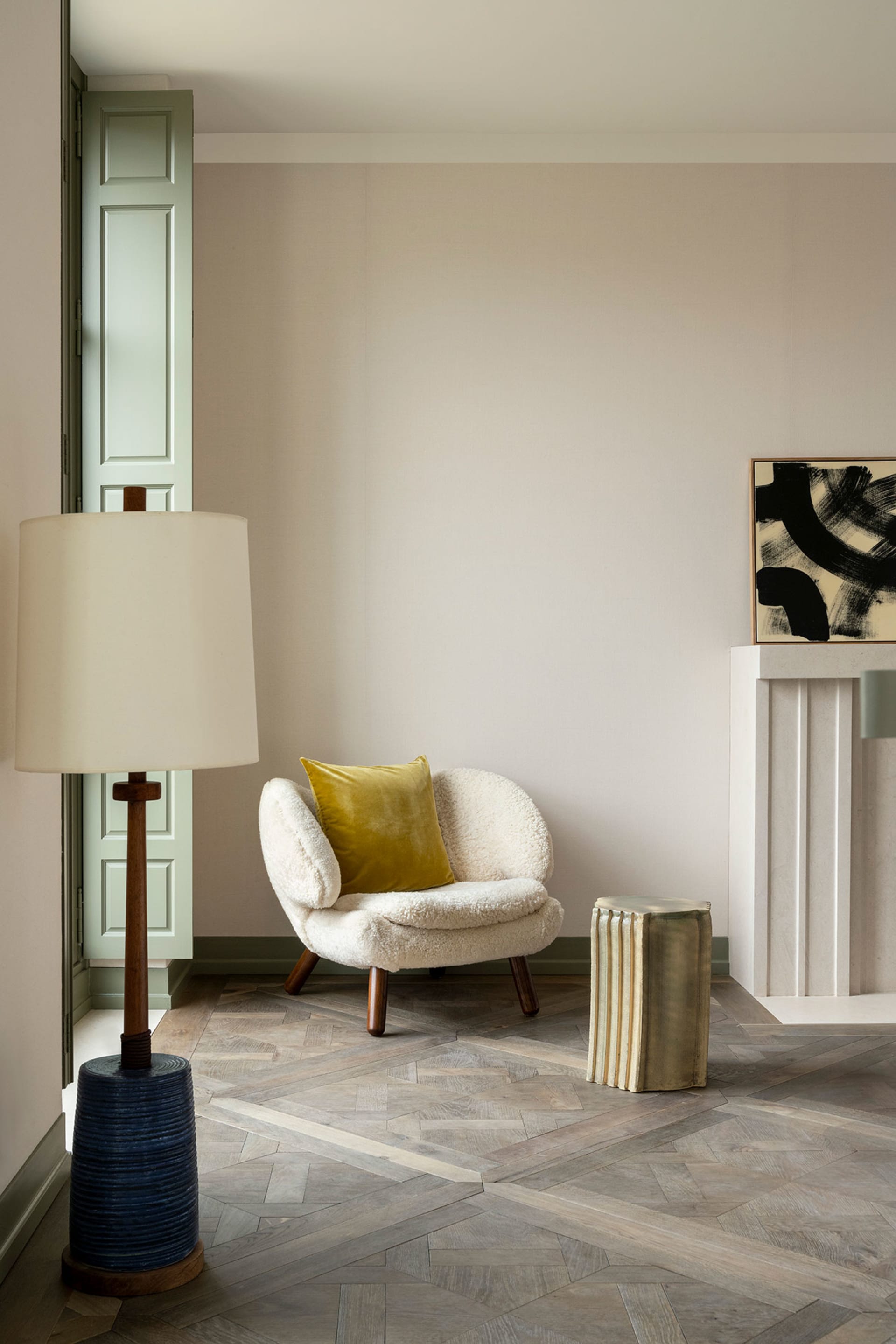 A cozy living room with a white armchair and mustard yellow pillow, featuring a wooden floor and a door in pastel green.