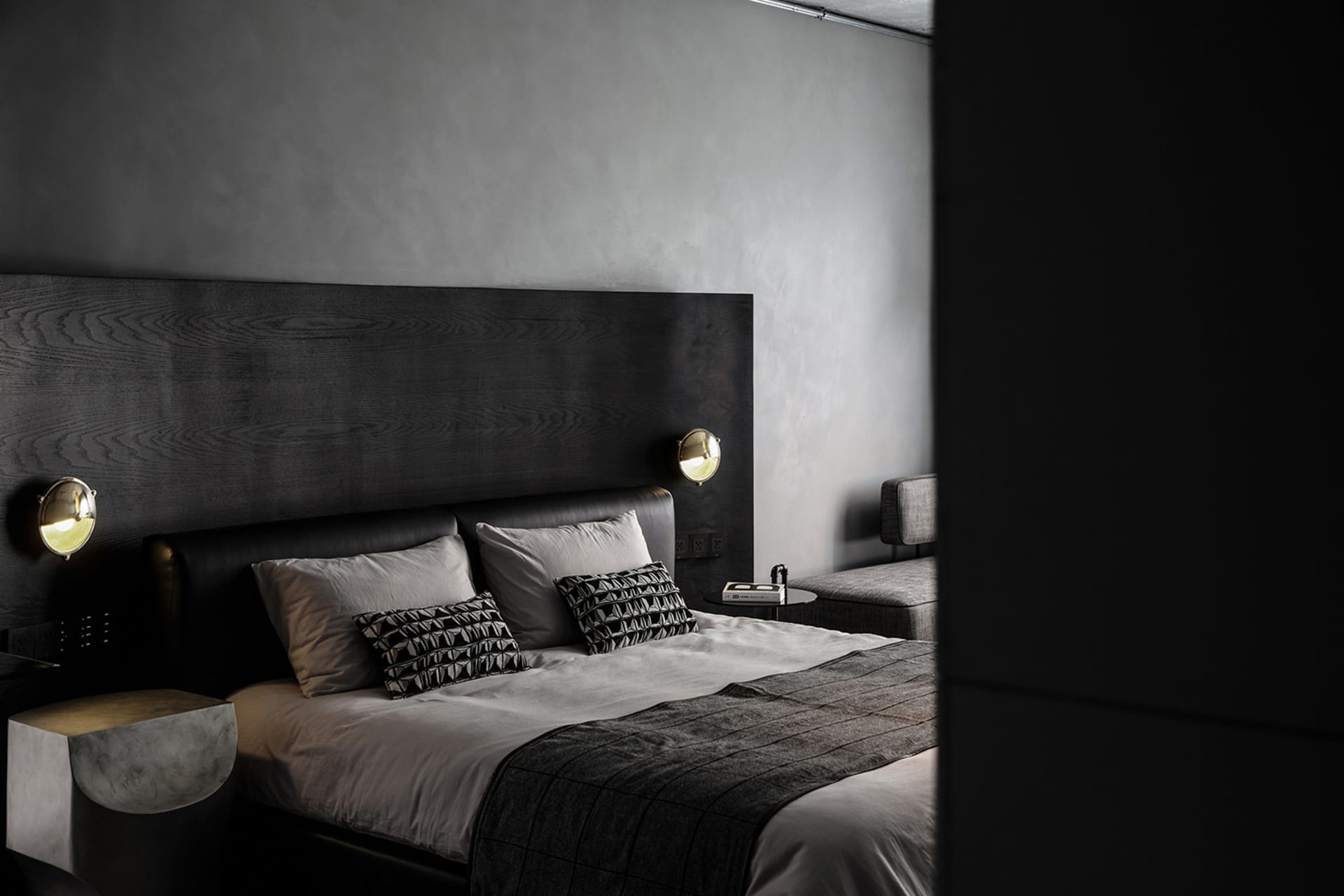 A minimalist bedroom with a dark wood headboard and light bedding, featuring modern sconce lighting and a sleek, low-profile
