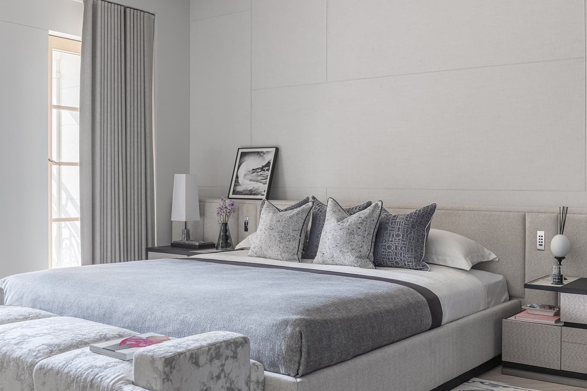 Modern minimalistic bedroom featuring upholstered furniture, neutral color palette, and abstract artwork.