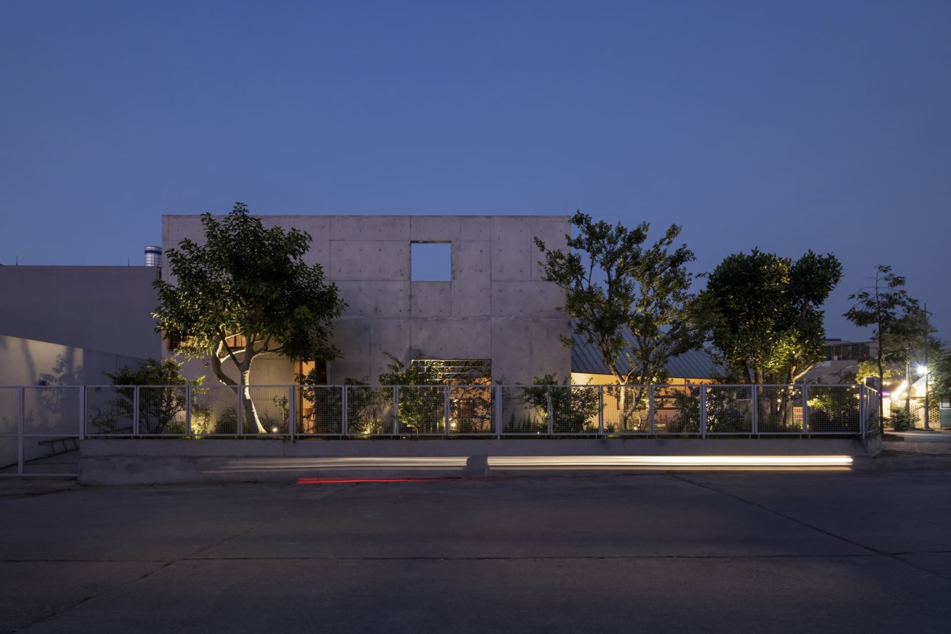 A modern building with a concrete exterior at night, featuring a large open window and trees.