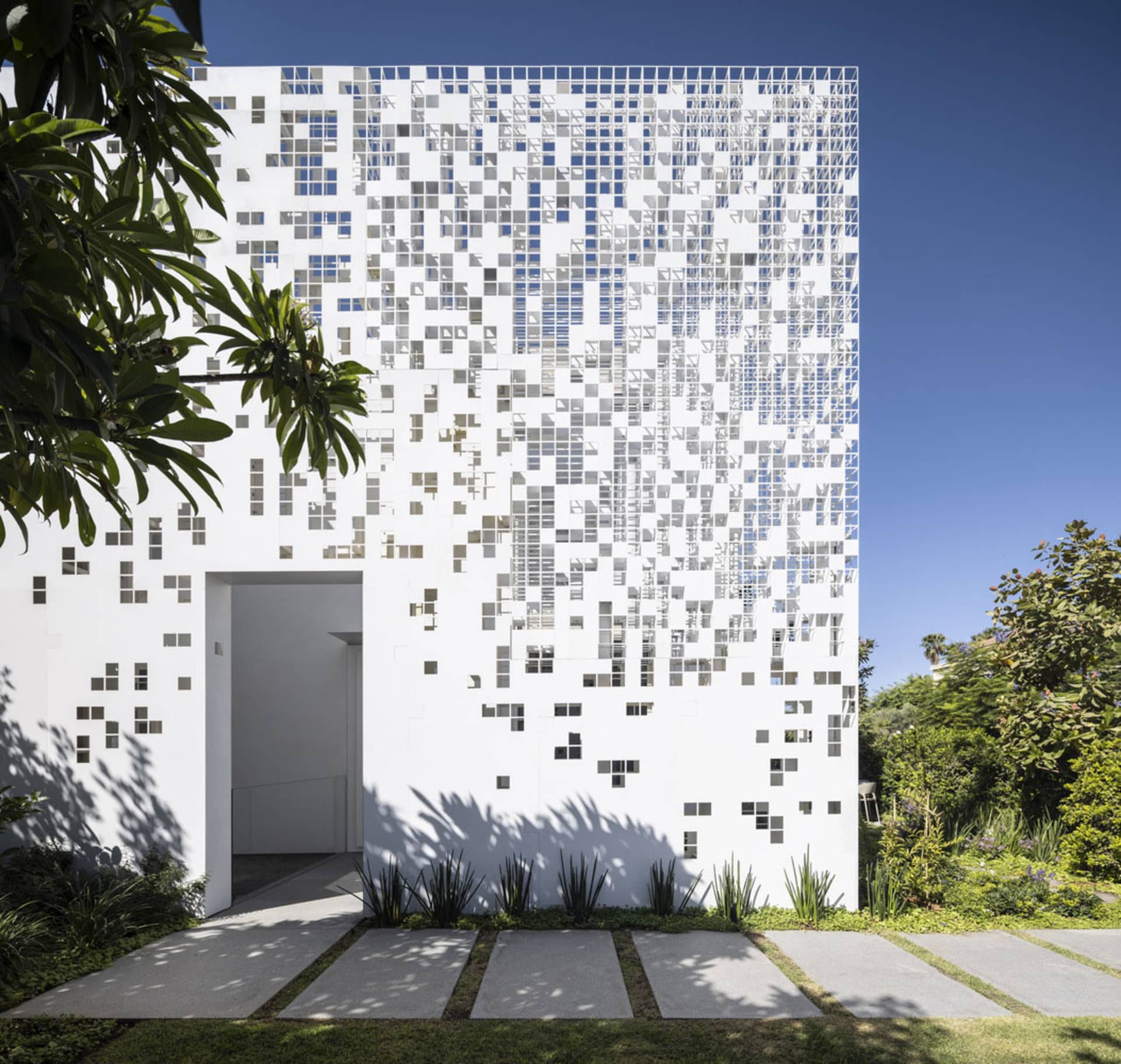 Modern building exterior featuring glass tiles with a white and gray pattern, set against a clear blue sky with landscaped gr