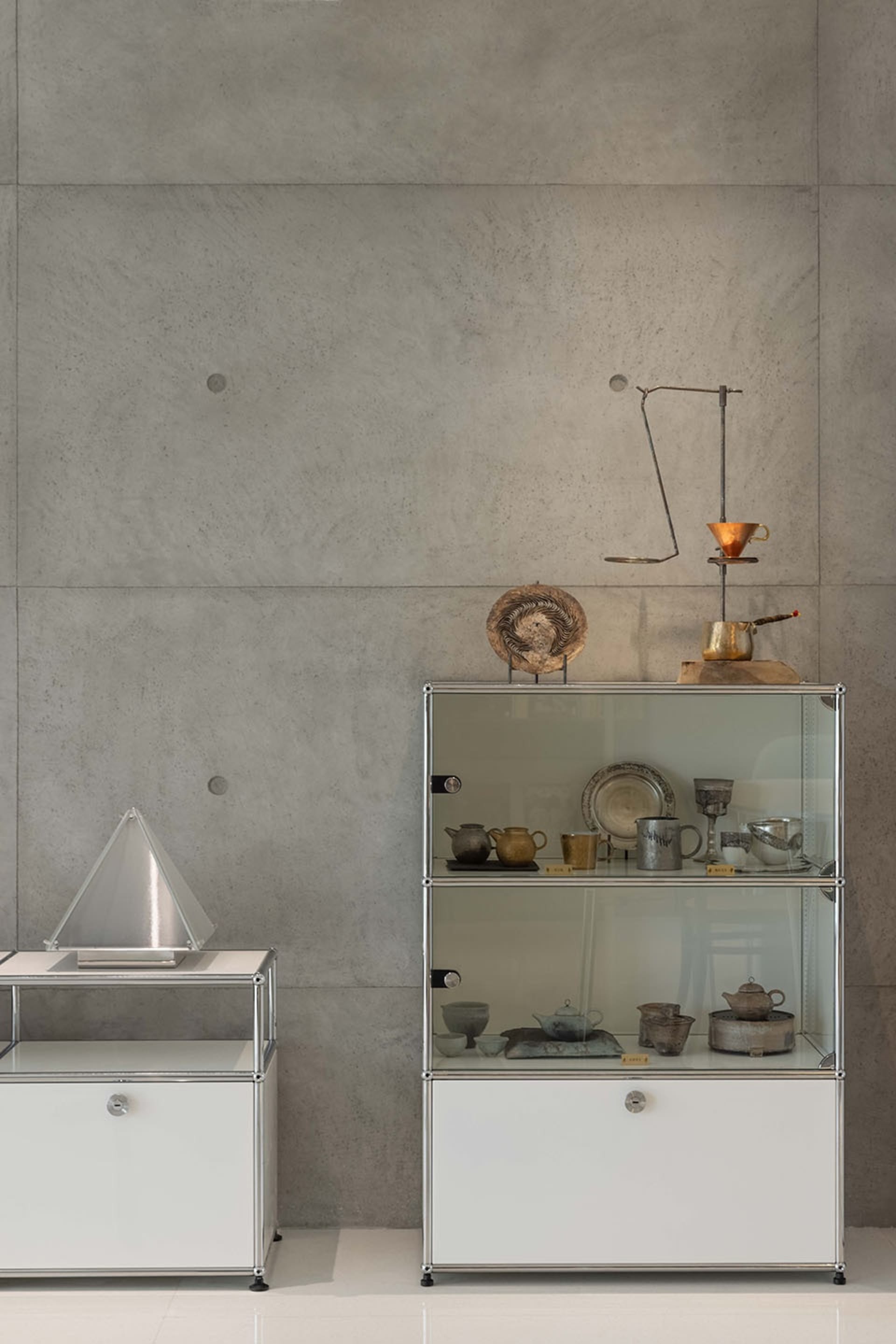 A display case featuring various metal objects, including bowls, plates, and vases, against a concrete wall.