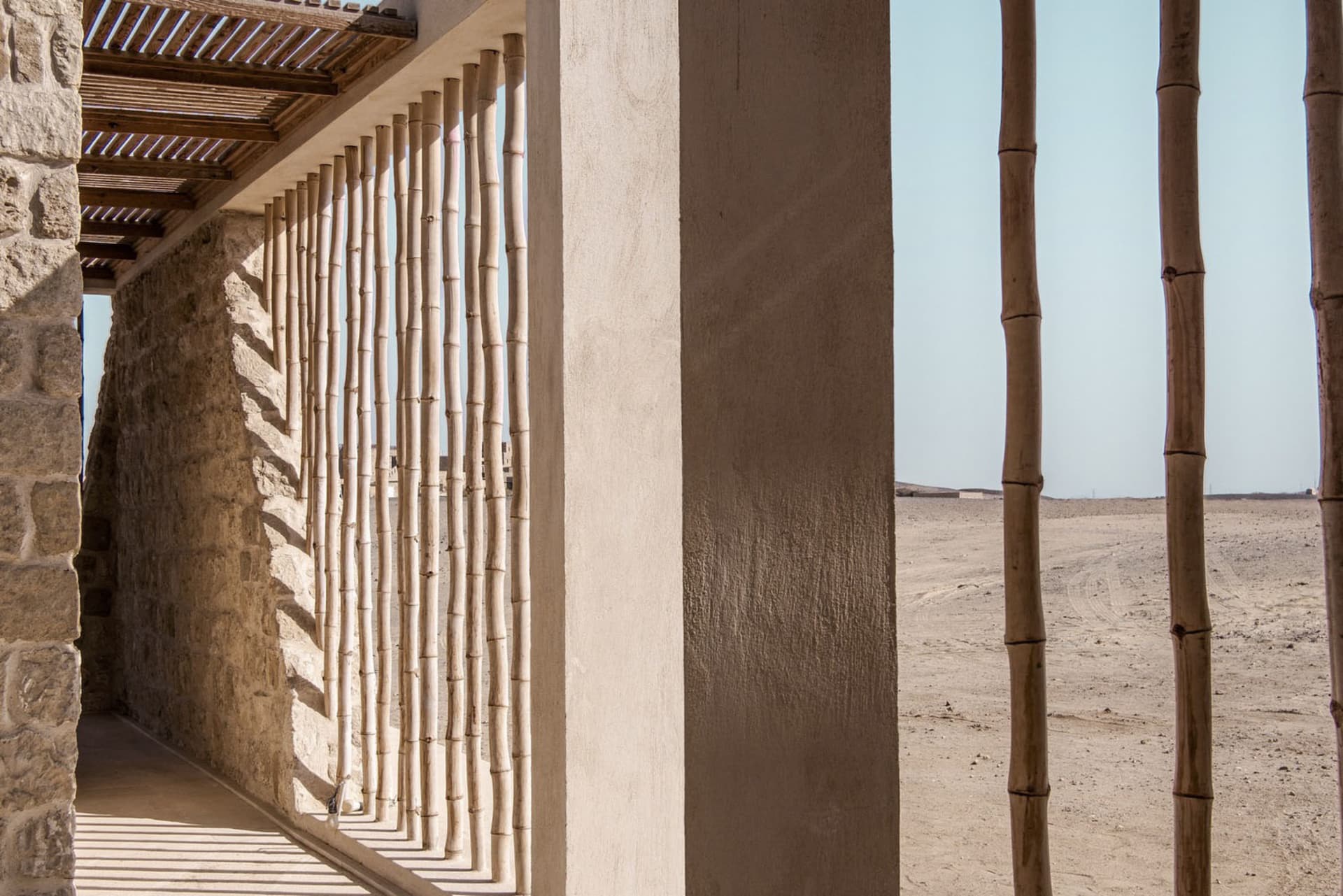 A wooden frame with stone walls extends from a desert-rimmed beach, showcasing the structure of a house.
