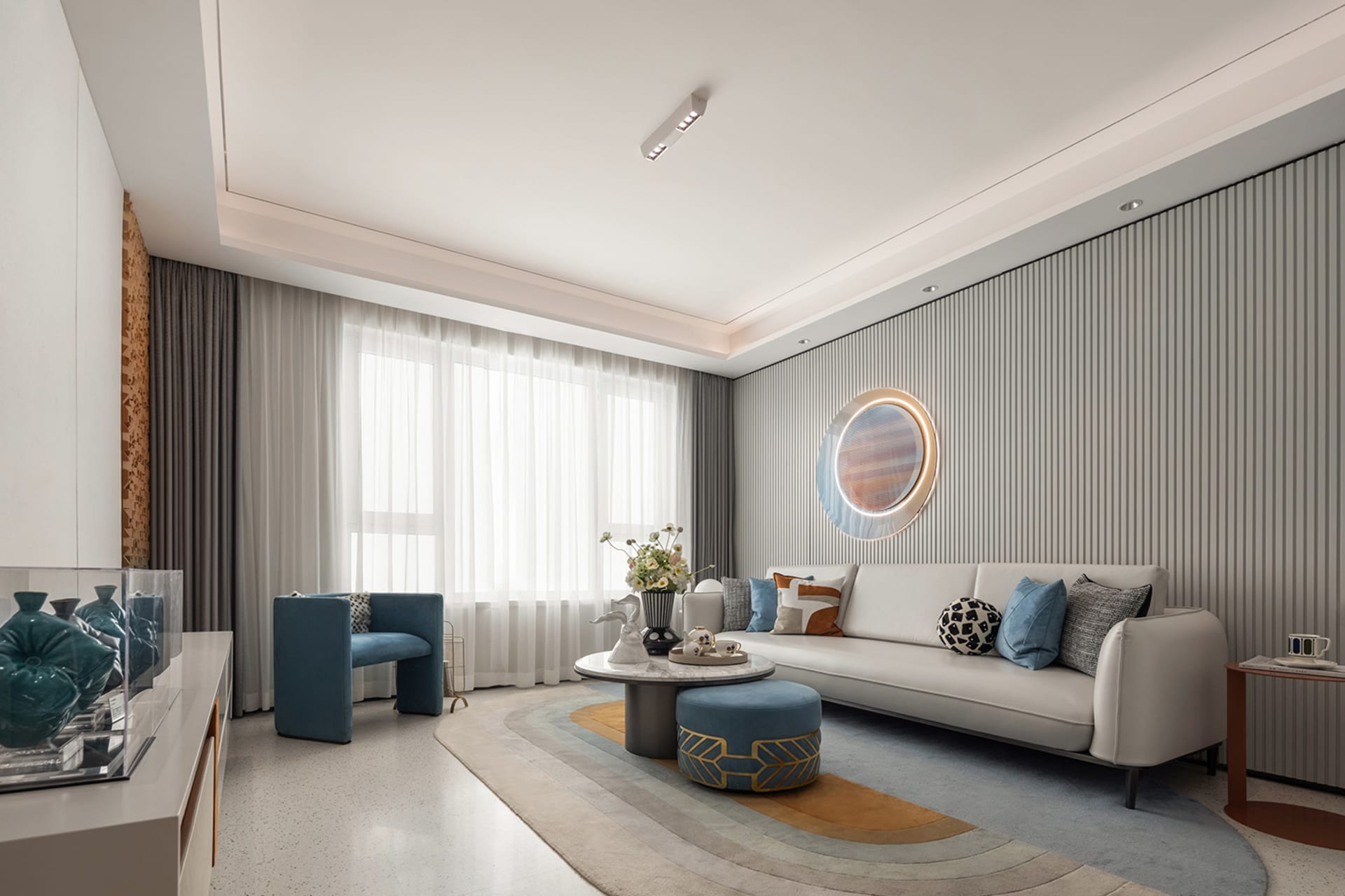 A stylish, modern living room with minimalist decor, featuring a white sofa, blue chair, and textured rug.