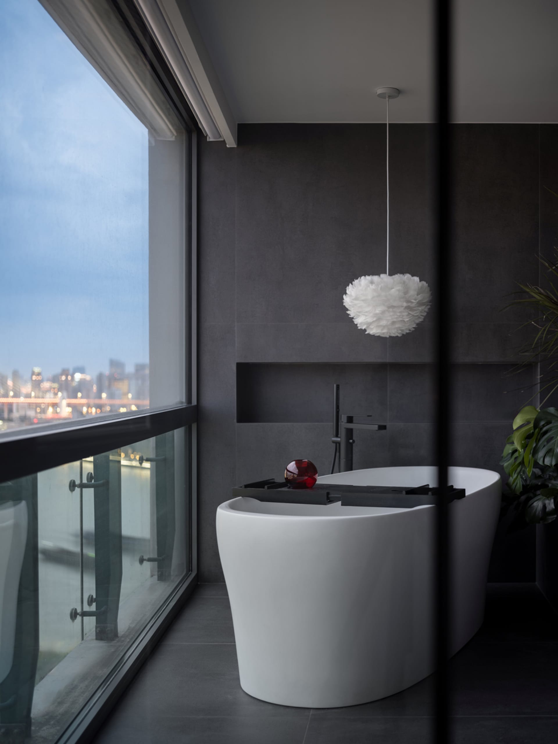 Modern bathroom featuring a freestanding bathtub made of white concrete with a red object on a tray and a white pendant lamp
