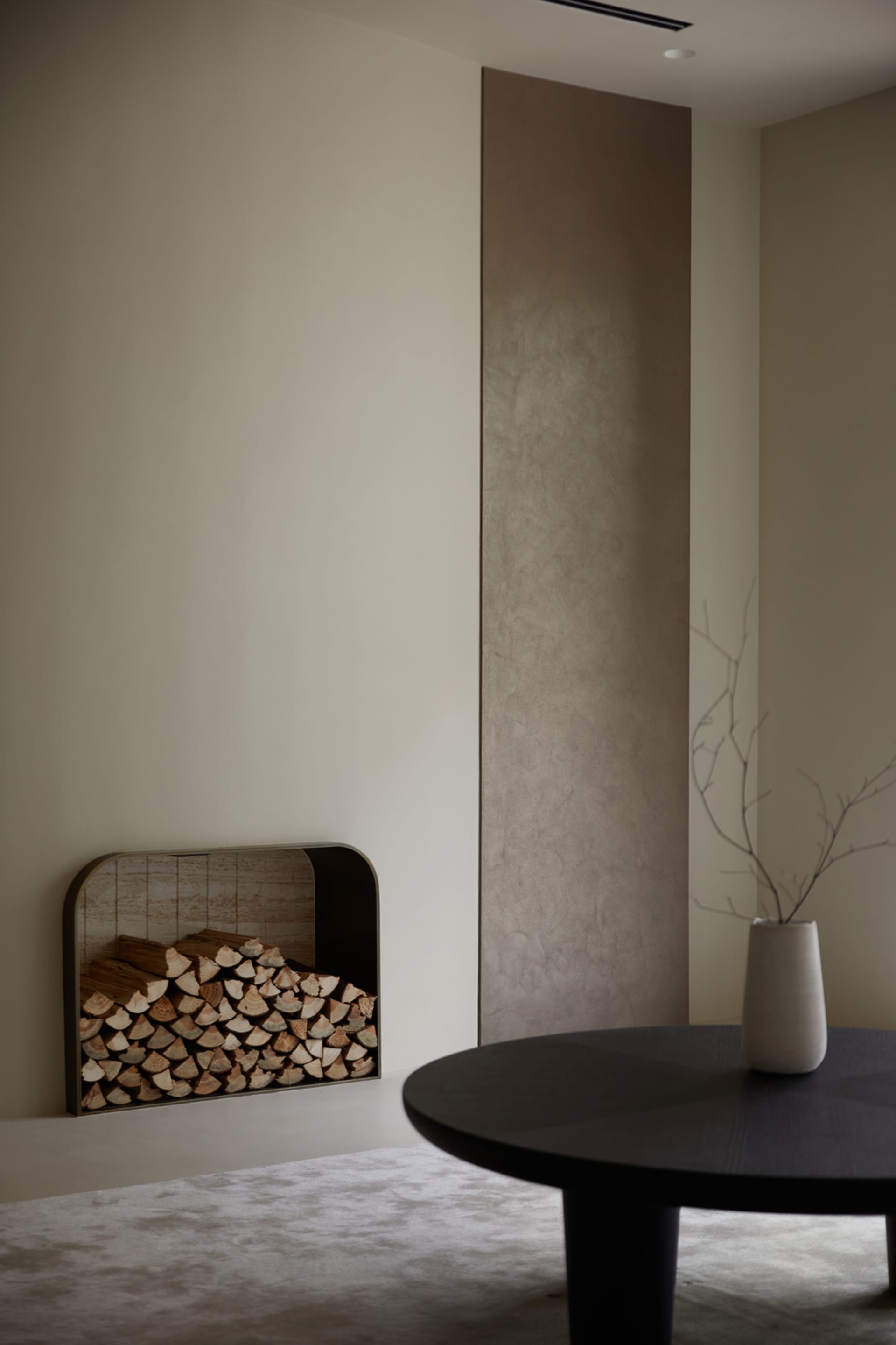 A minimalist living room featuring a round wooden table and a modern fireplace.