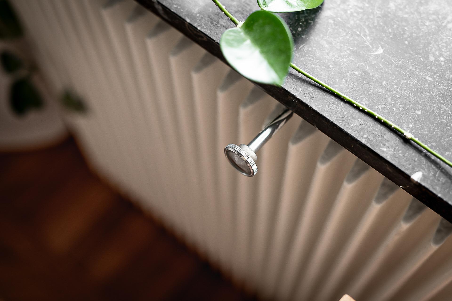 A metallic radiator handle with a green leaf attached to it, placed against a white radiator.